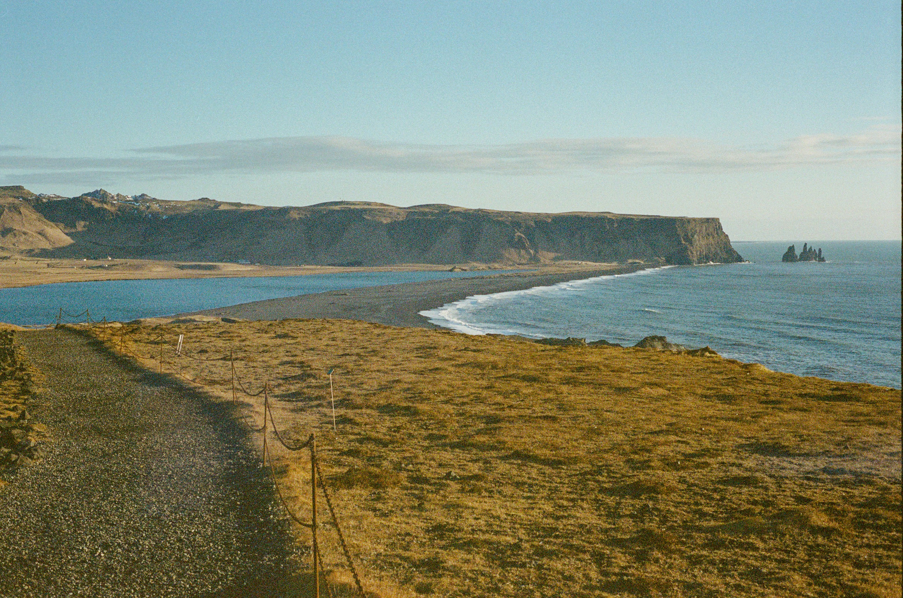 Scenic coastal view with black sand beach and distant cliffs.