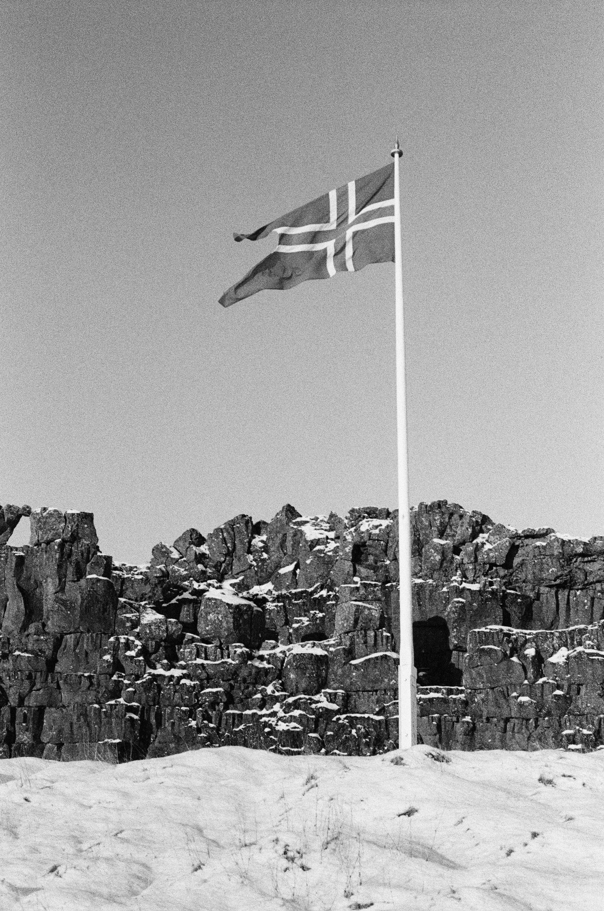 Norwegian flag flies over snowy rocky landscape.