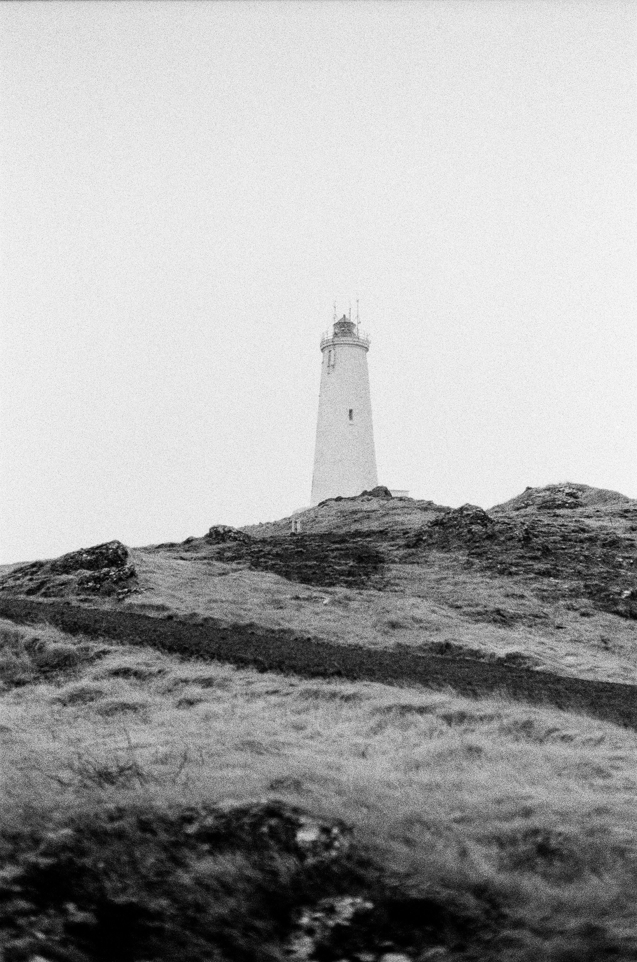 A lighthouse stands on a grassy hill.