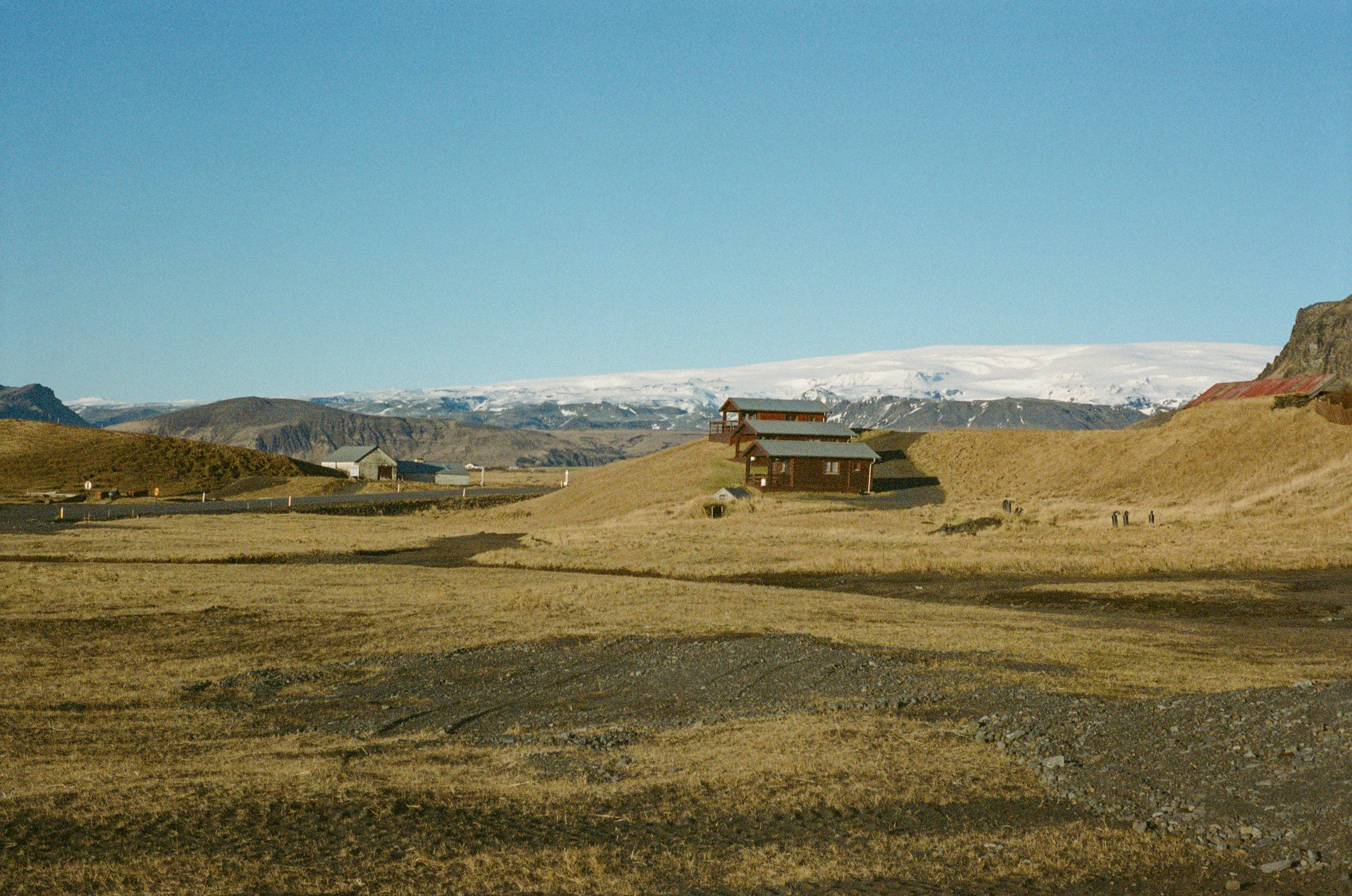 Wooden cabins in a dry landscape with snow-capped mountains.