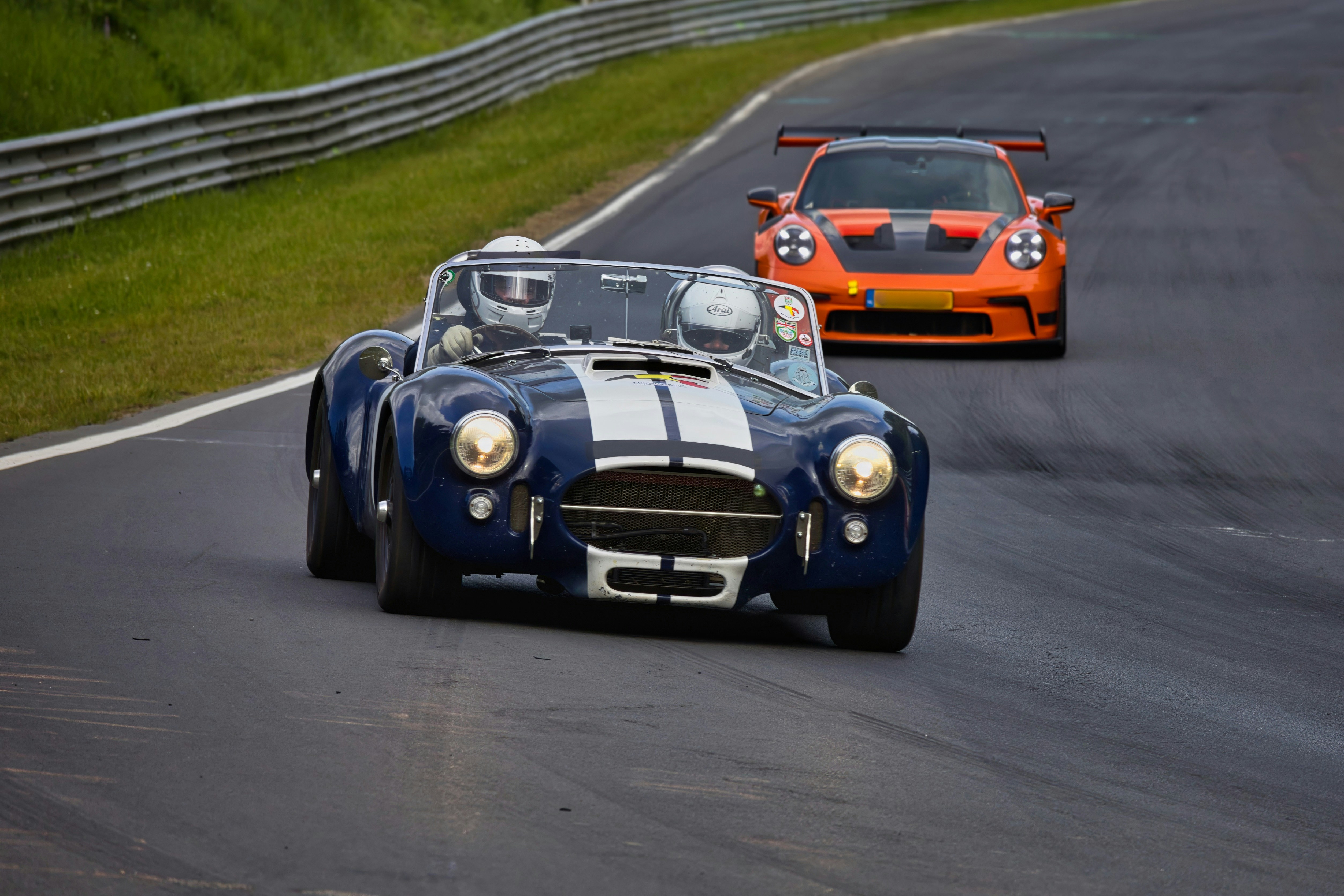 Classic blue and modern orange sports cars racing on track.