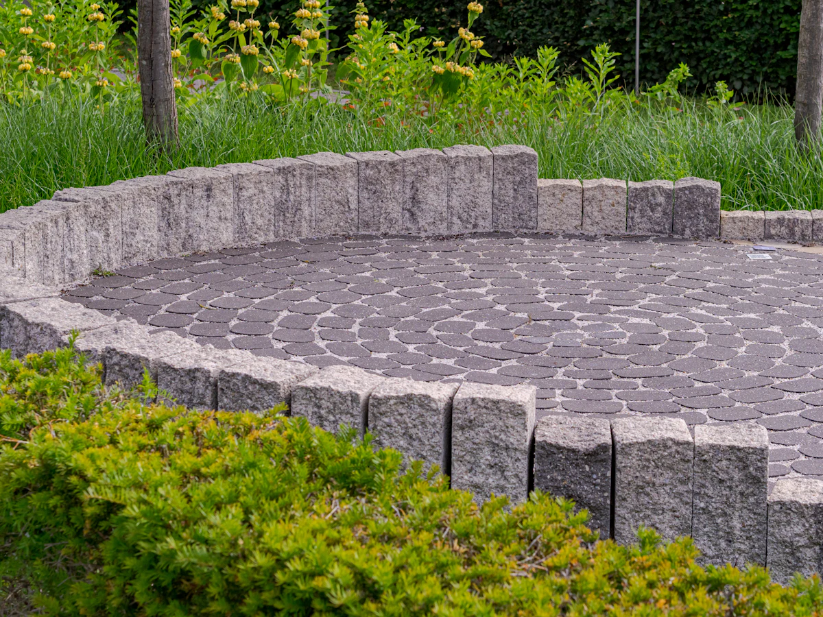 A paver patio with a low stone wall and shrubs