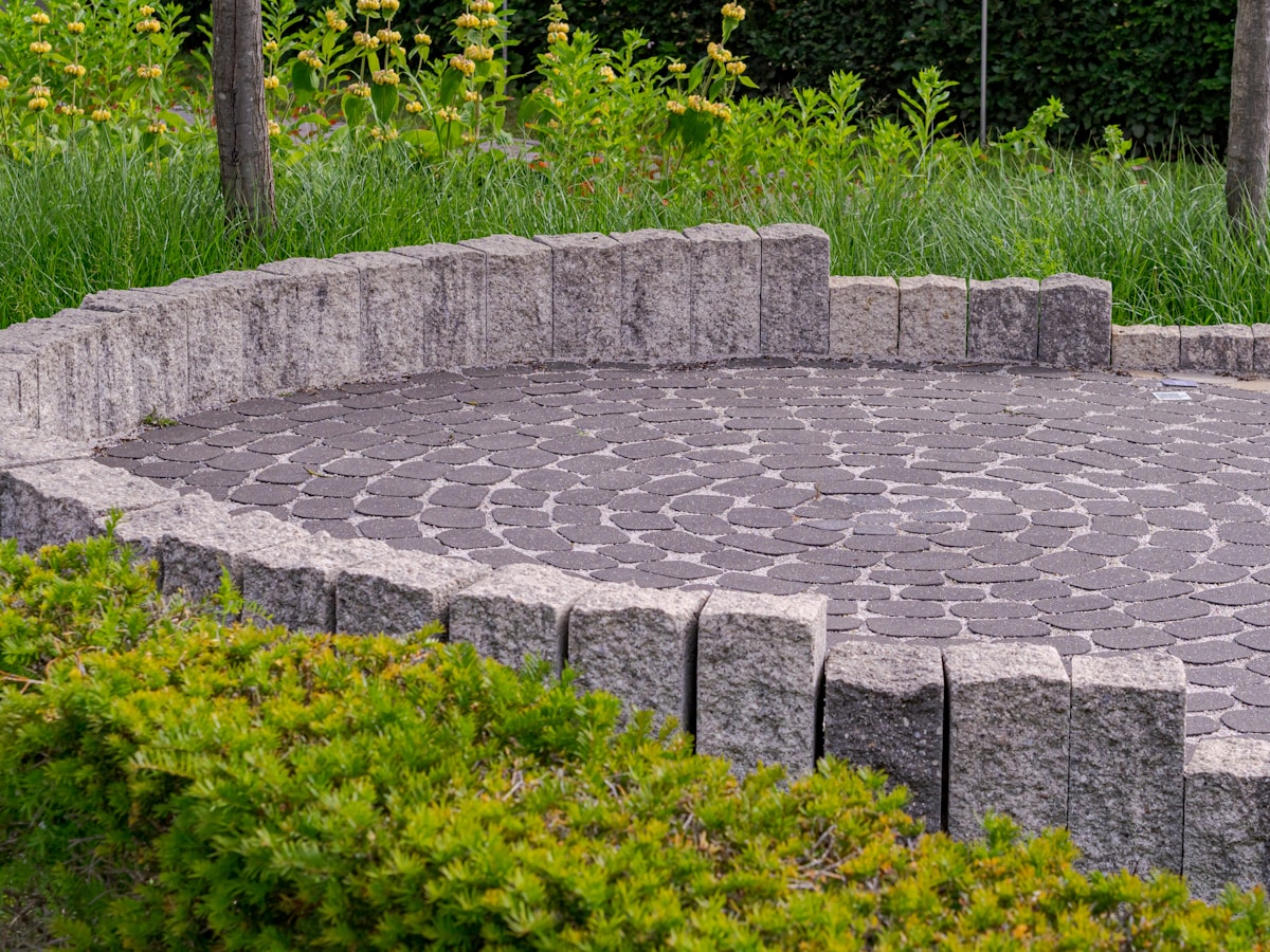 Circular stone patio framed by a low seating wall and evergreen shrubs, designed as a garden room within a larger landscape