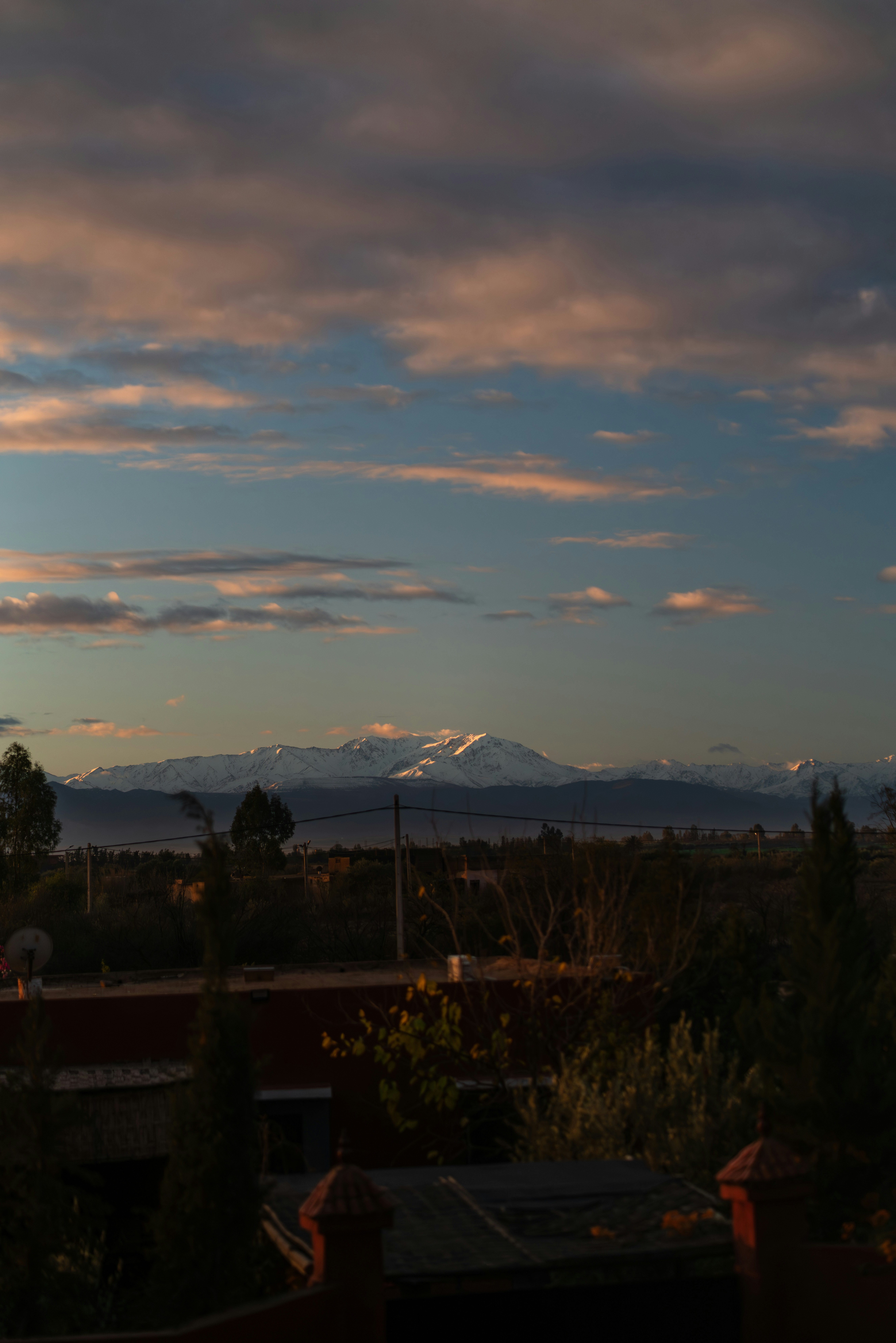 Snow-capped mountains under a colorful sunset sky with foreground buildings.
