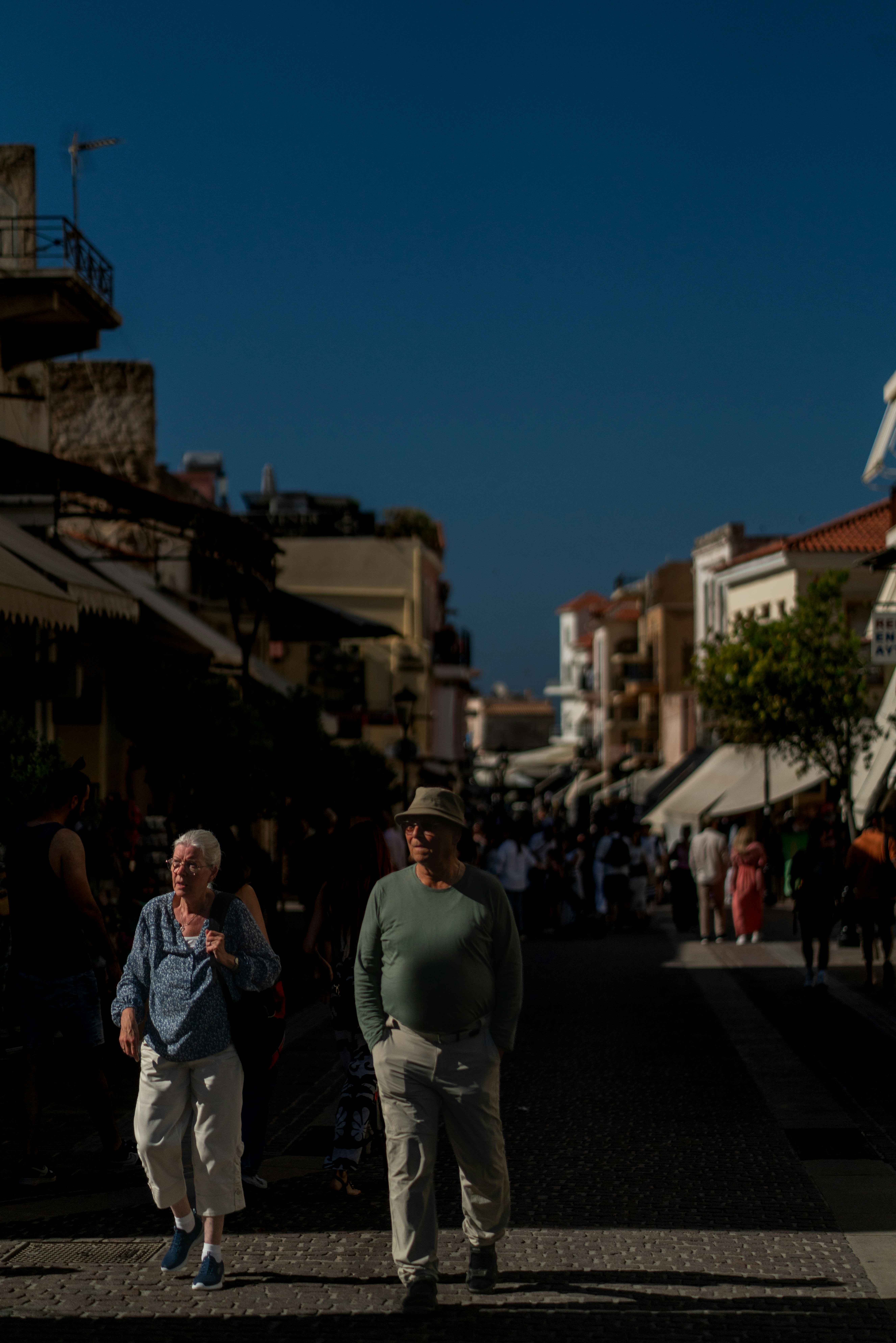 Two elderly people walk down a sunny town street.