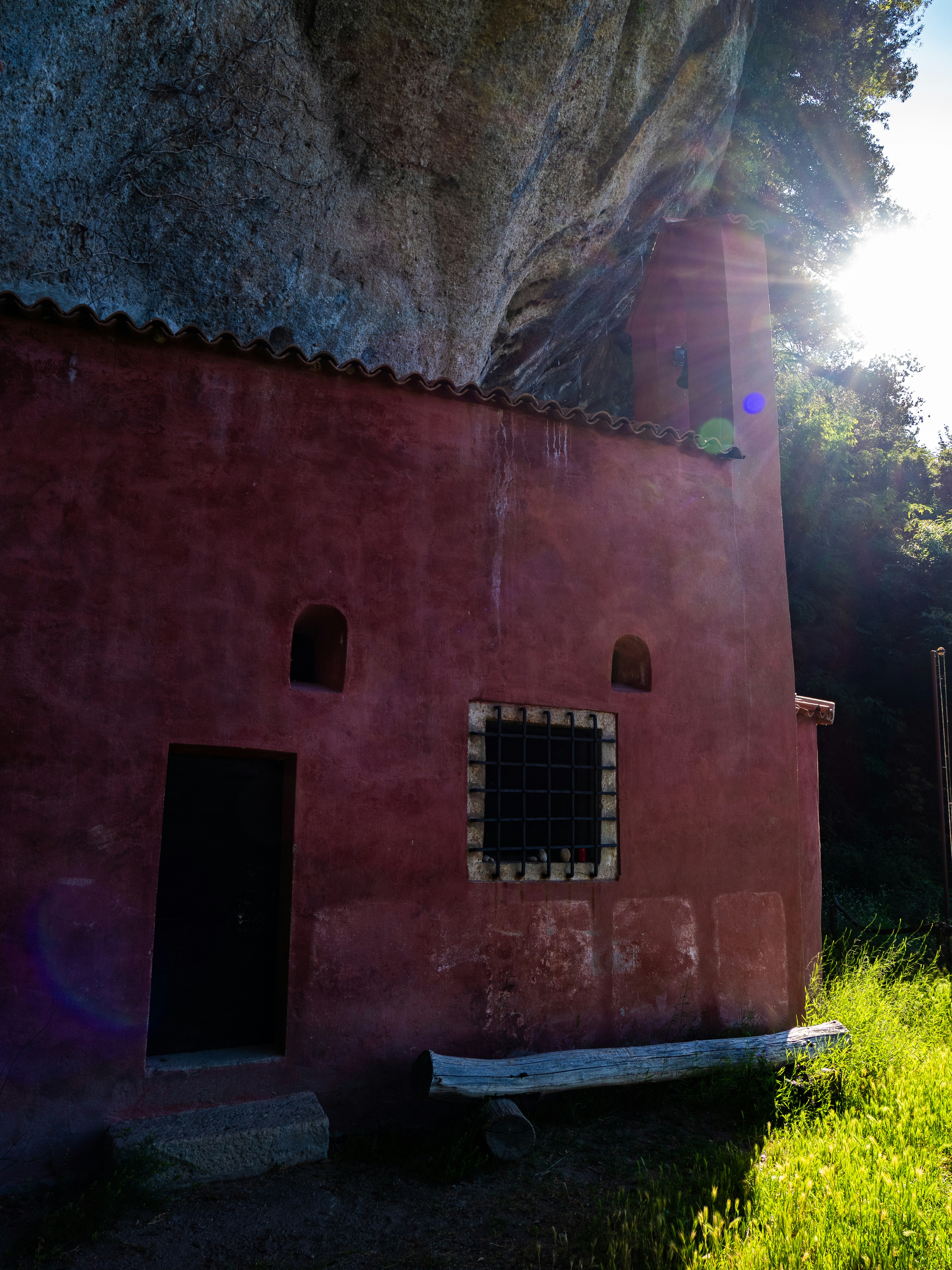 Sunlight illuminates a red chapel built into a cliffside.