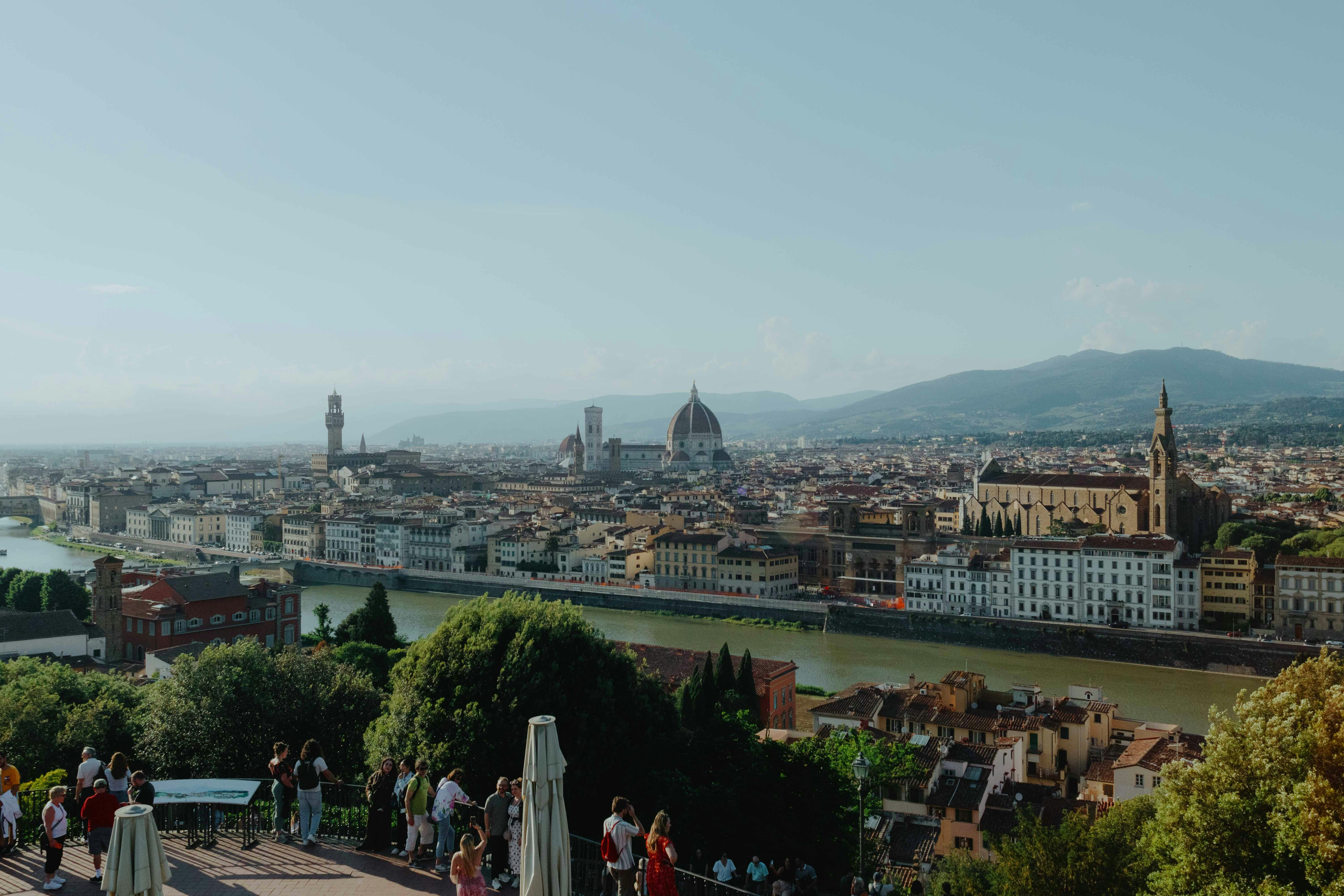 Florence cityscape with river, historic buildings, and distant hills.