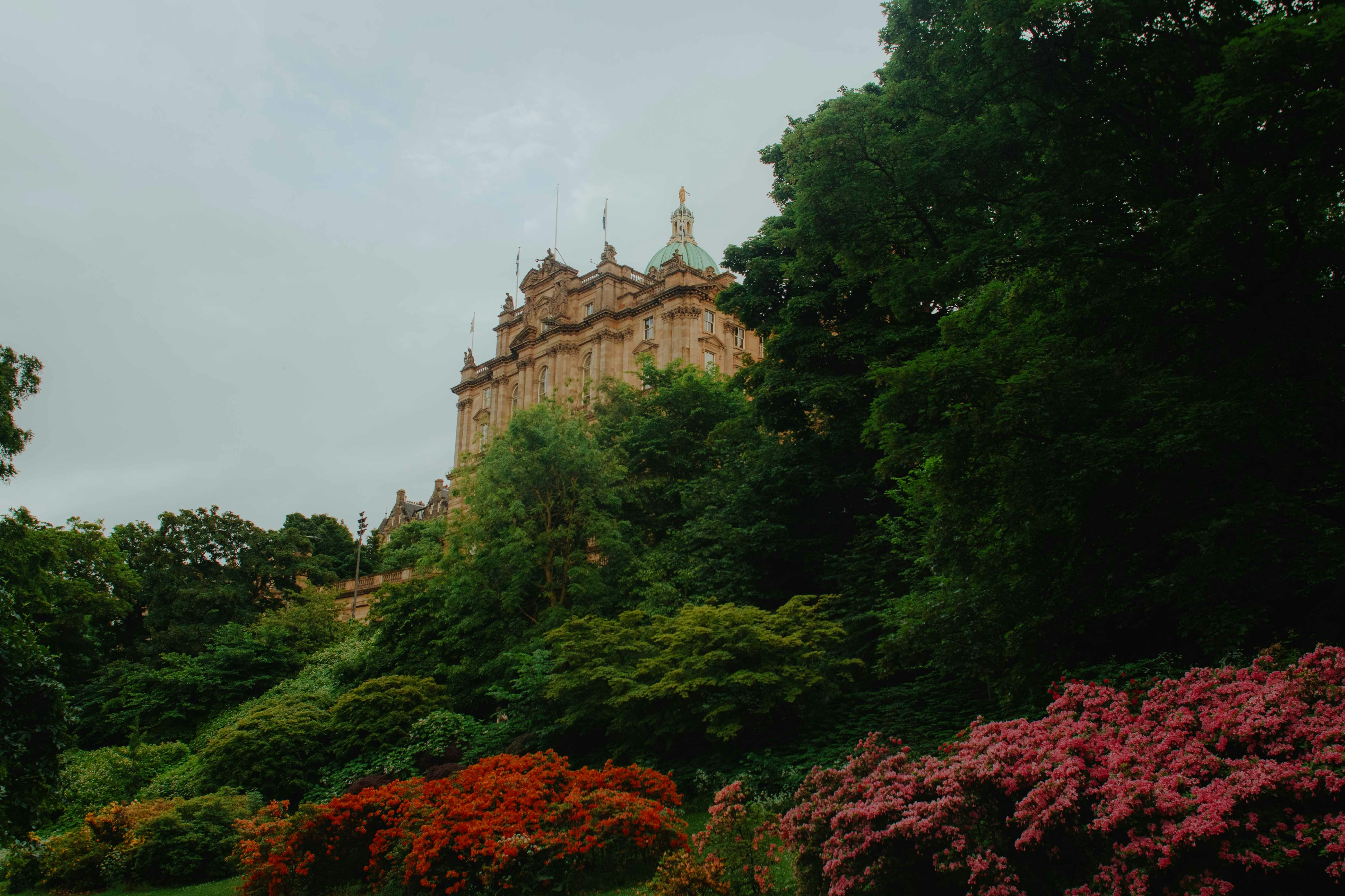 Ornate building partially hidden by lush trees and colorful bushes.