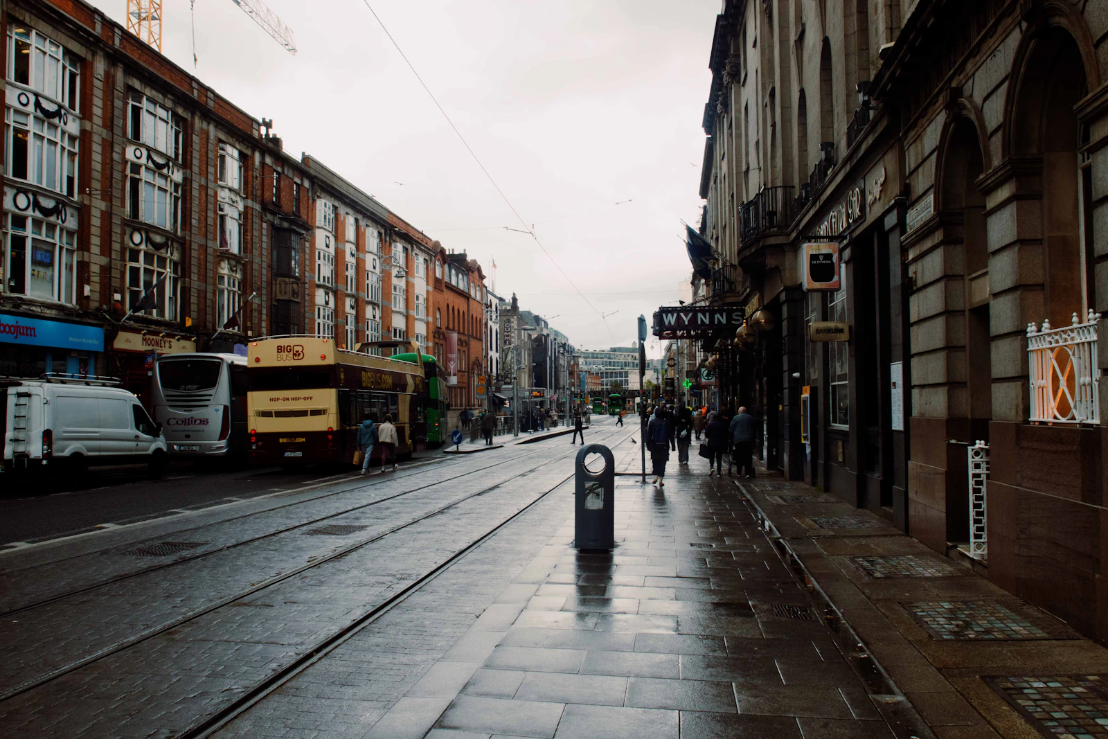 Wet city street with buildings, a bus, and people walking.