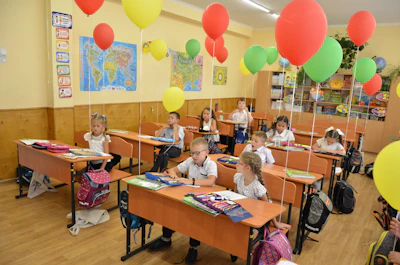 Children sitting at desks in a classroom decorated with balloons
