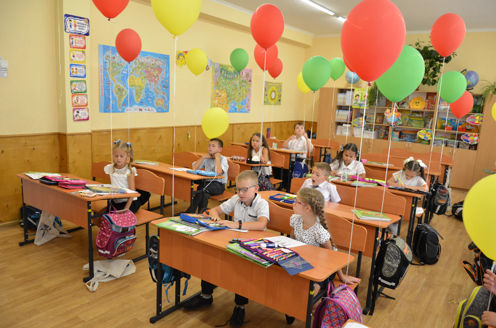 Young children at their desks in a classroom decorated with balloons for the first day of school