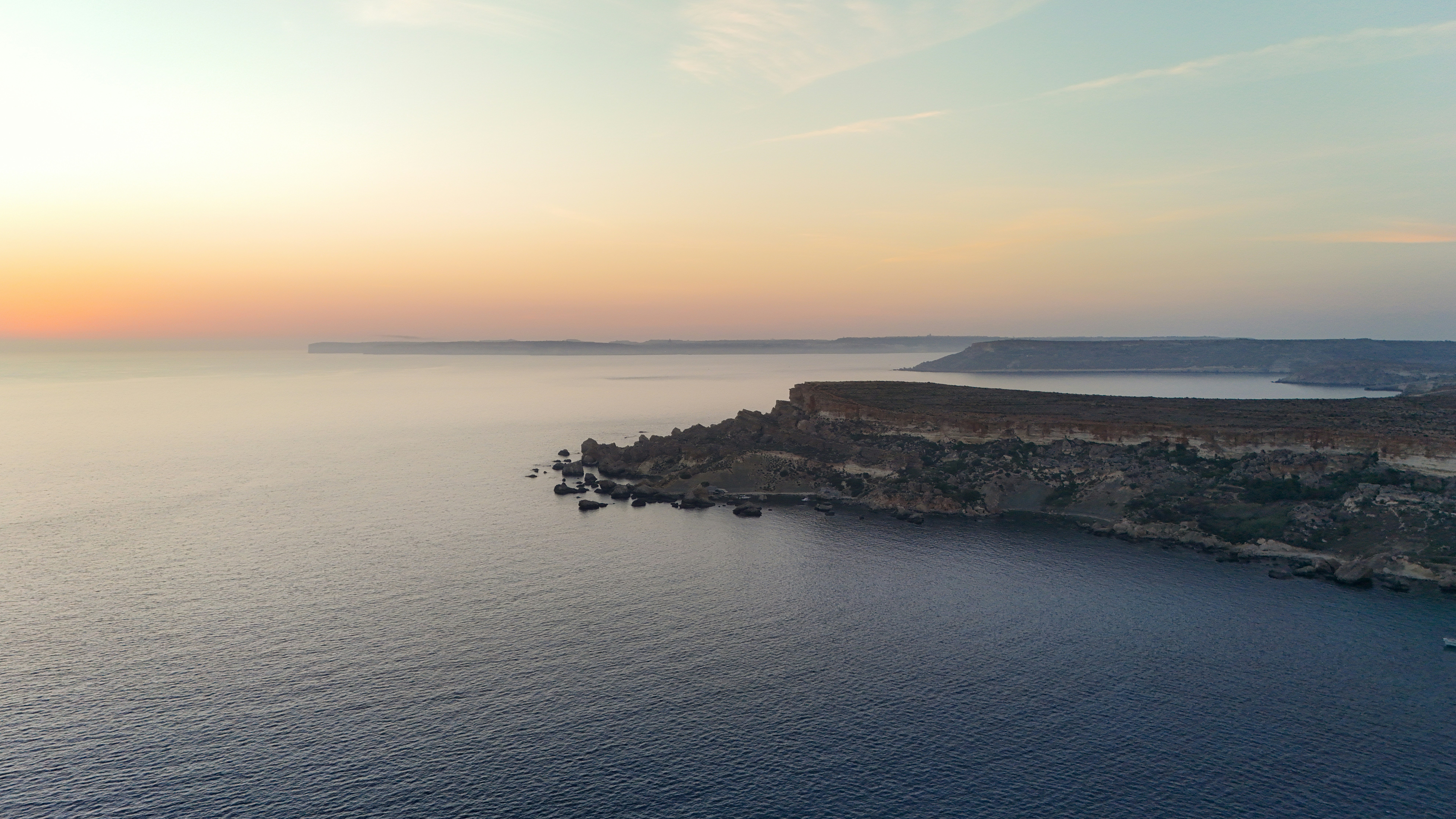 Sunrise over rugged coastal cliffs and tranquil blue sea.