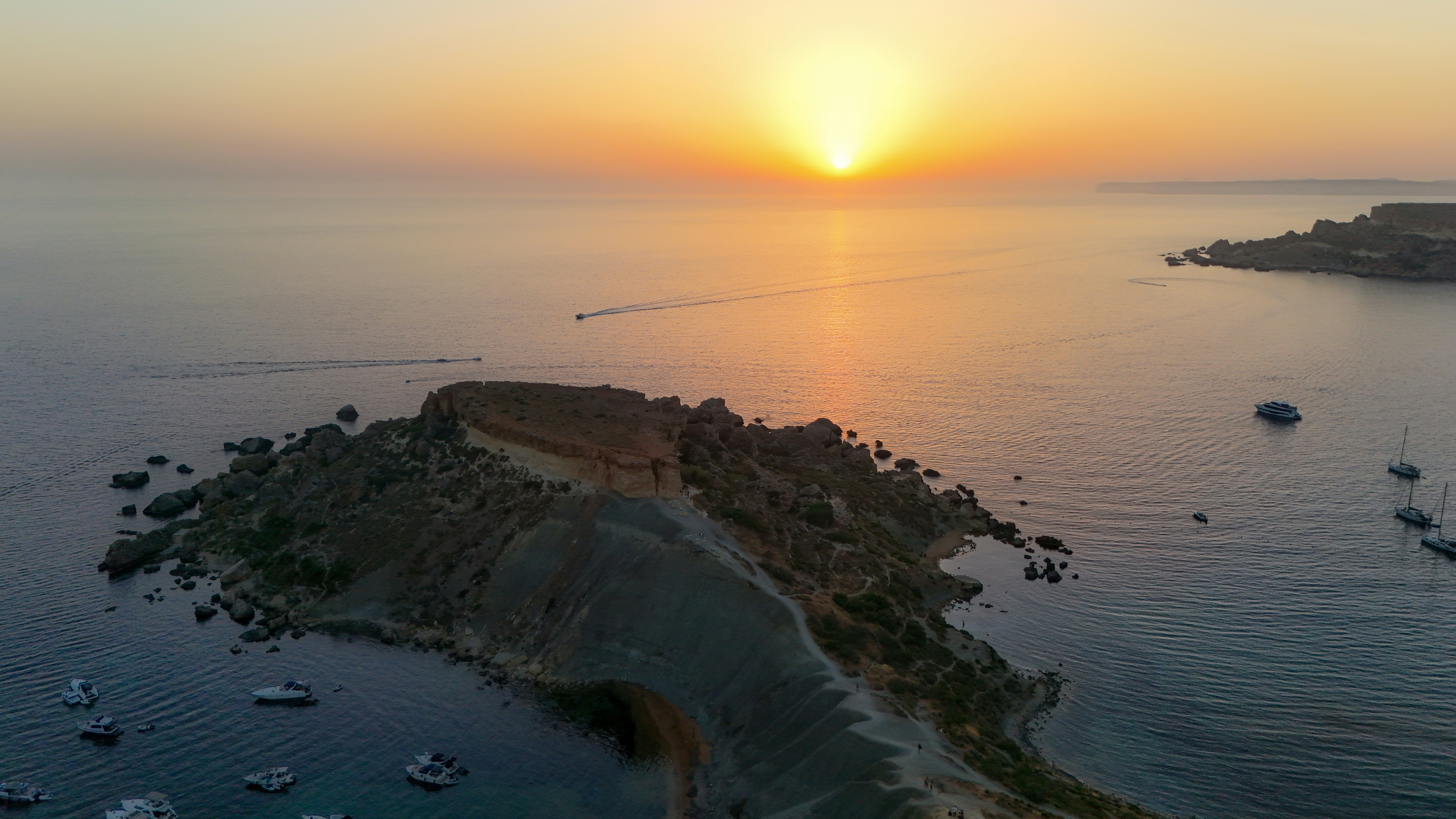 Sunset over an island with boats in the calm ocean.