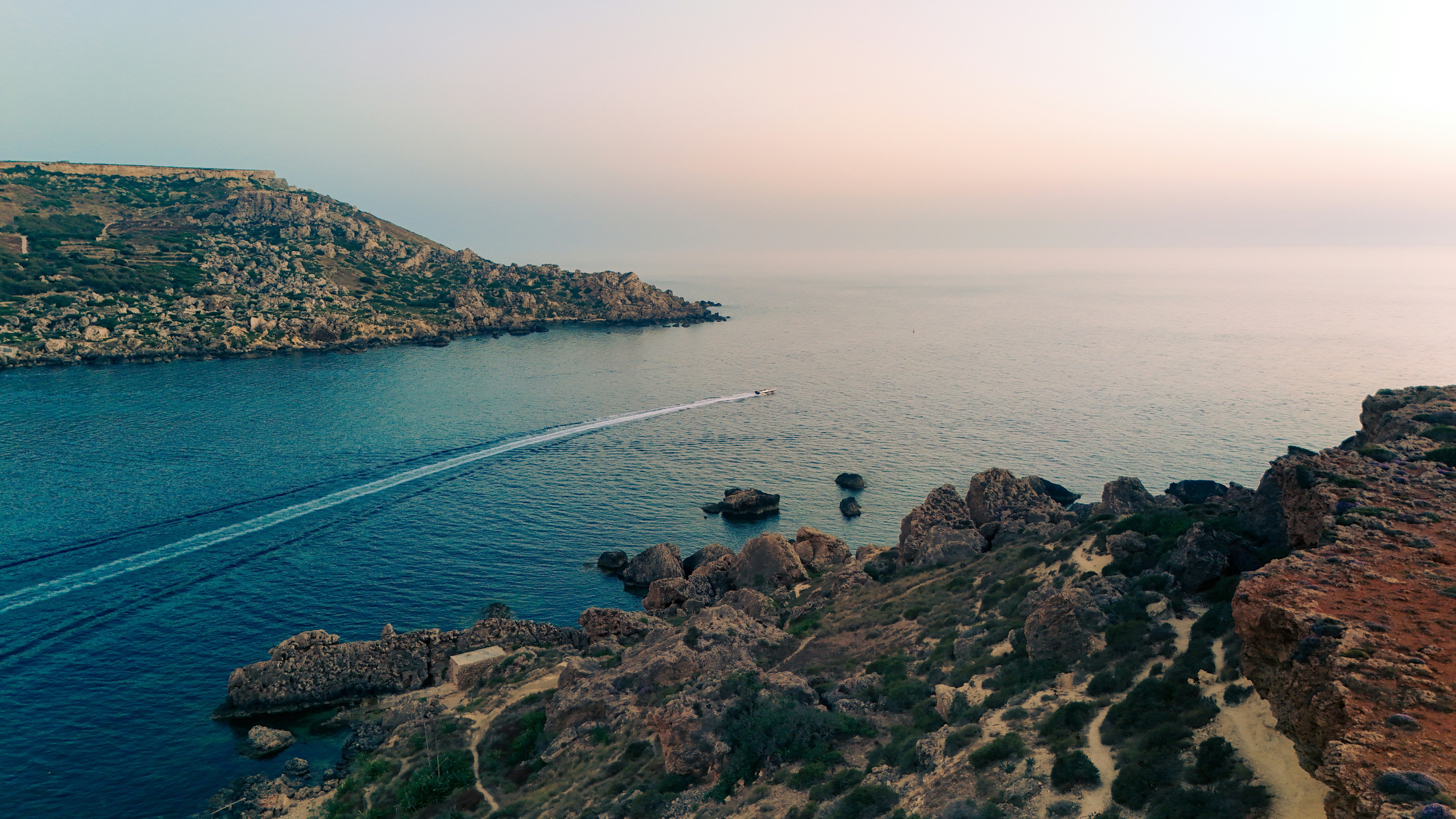 Boat on calm ocean near rocky coast at sunset.