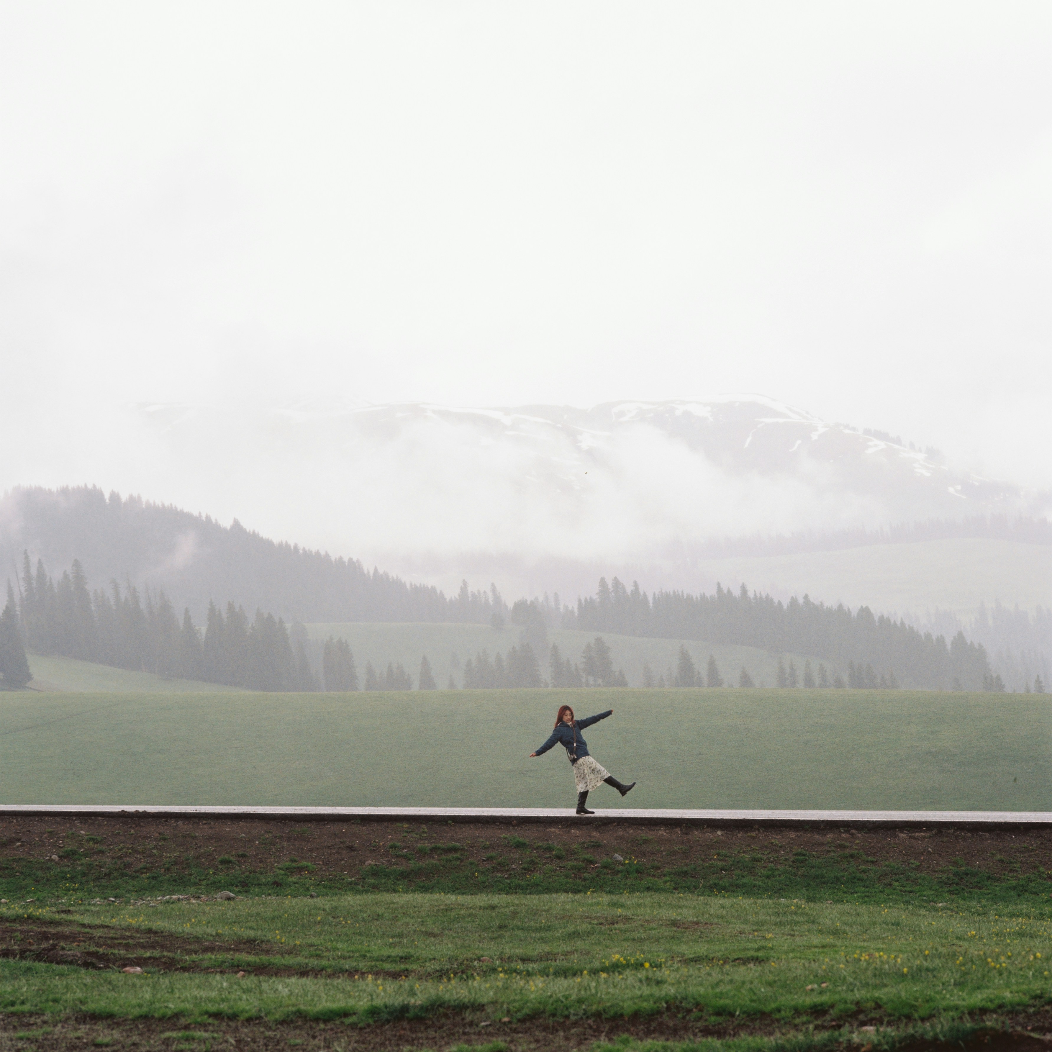 Person balancing on a road against a misty mountain landscape.