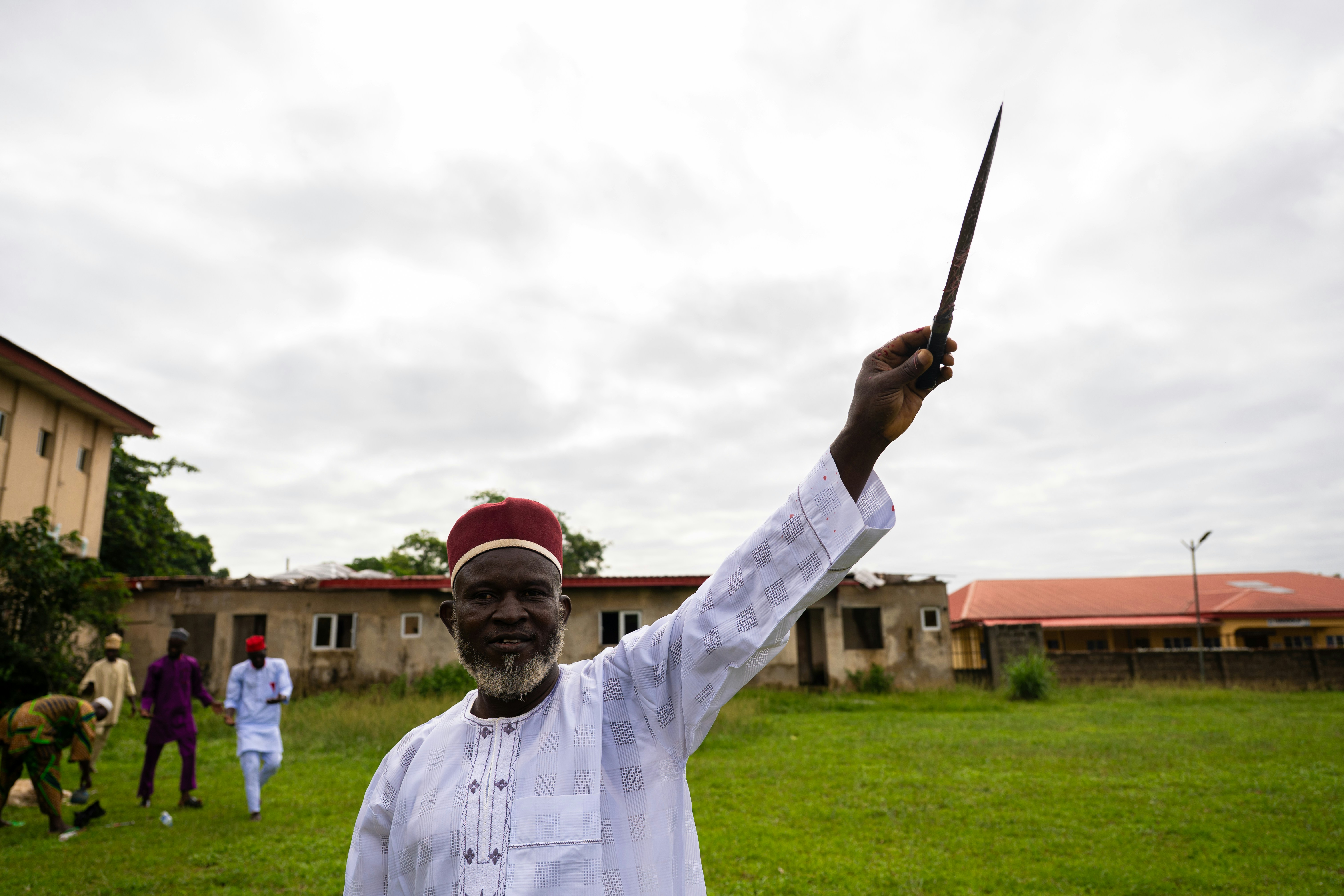 Elderly man in white robes points a stick skyward.
