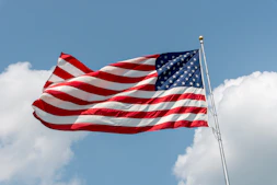 An american flag waving against a blue sky with clouds.