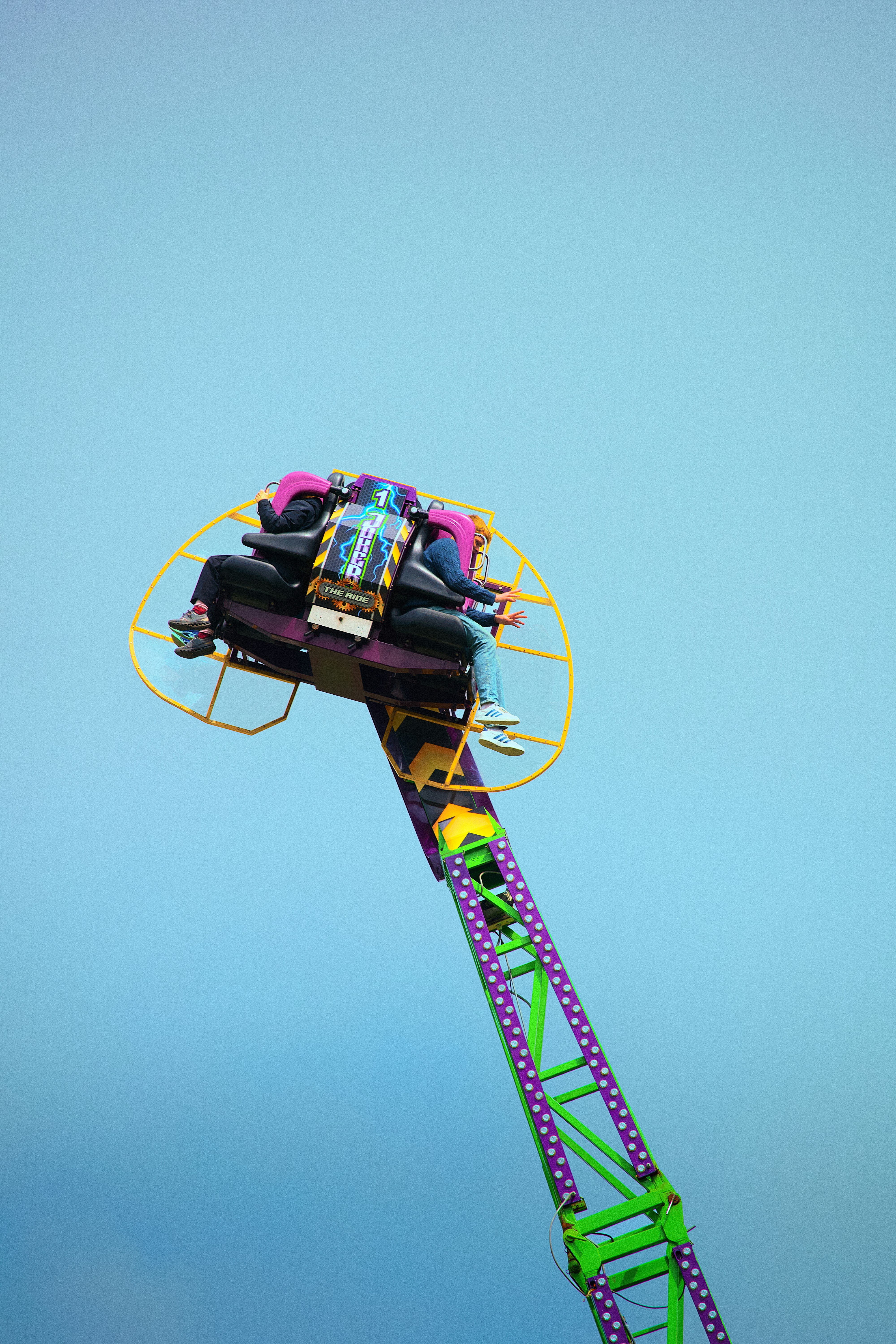 People enjoying a thrilling fairground ride against a blue sky.