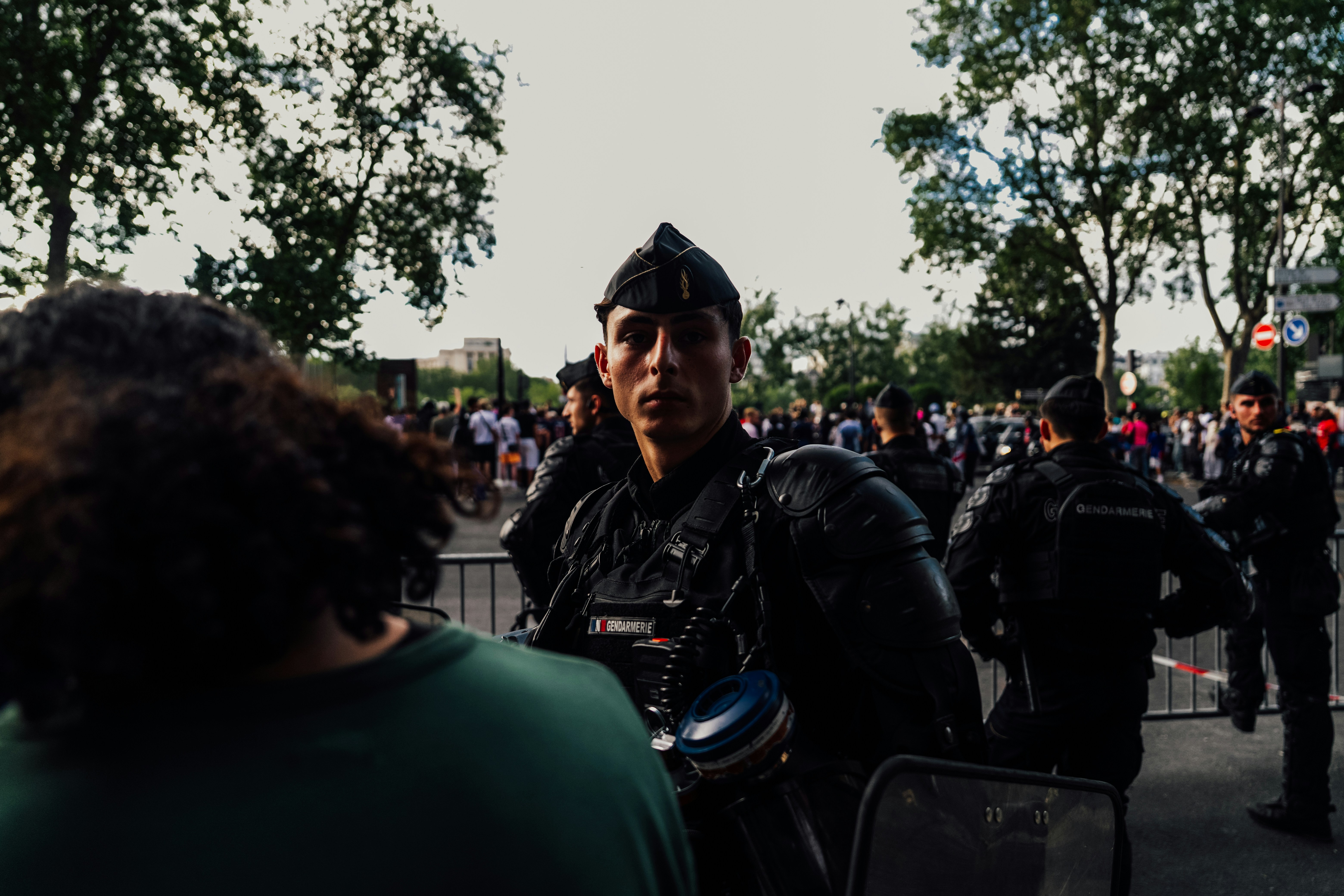 A uniformed officer stands in a crowd, looking forward.