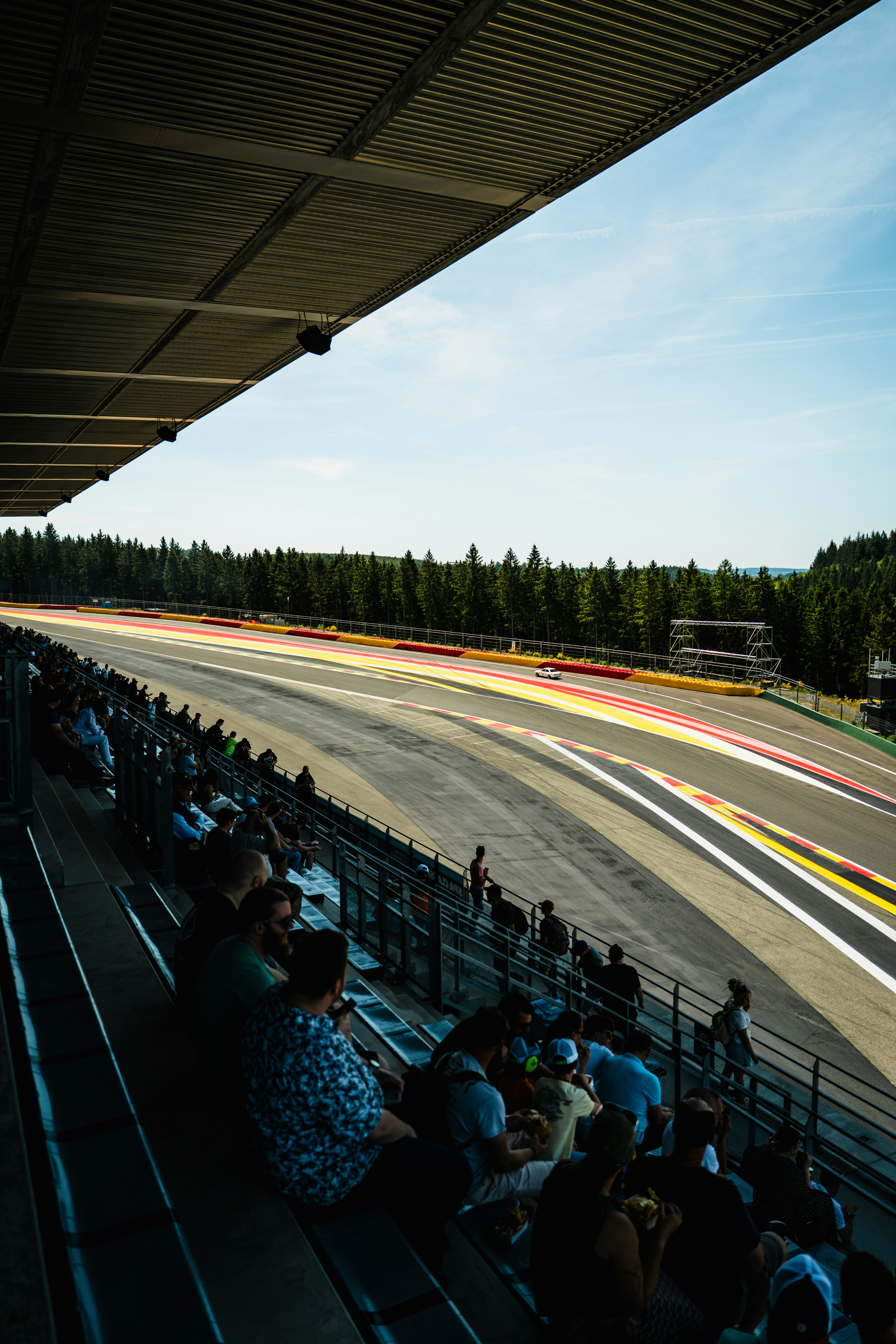 Spectators in grandstand watch blurred race cars on track.