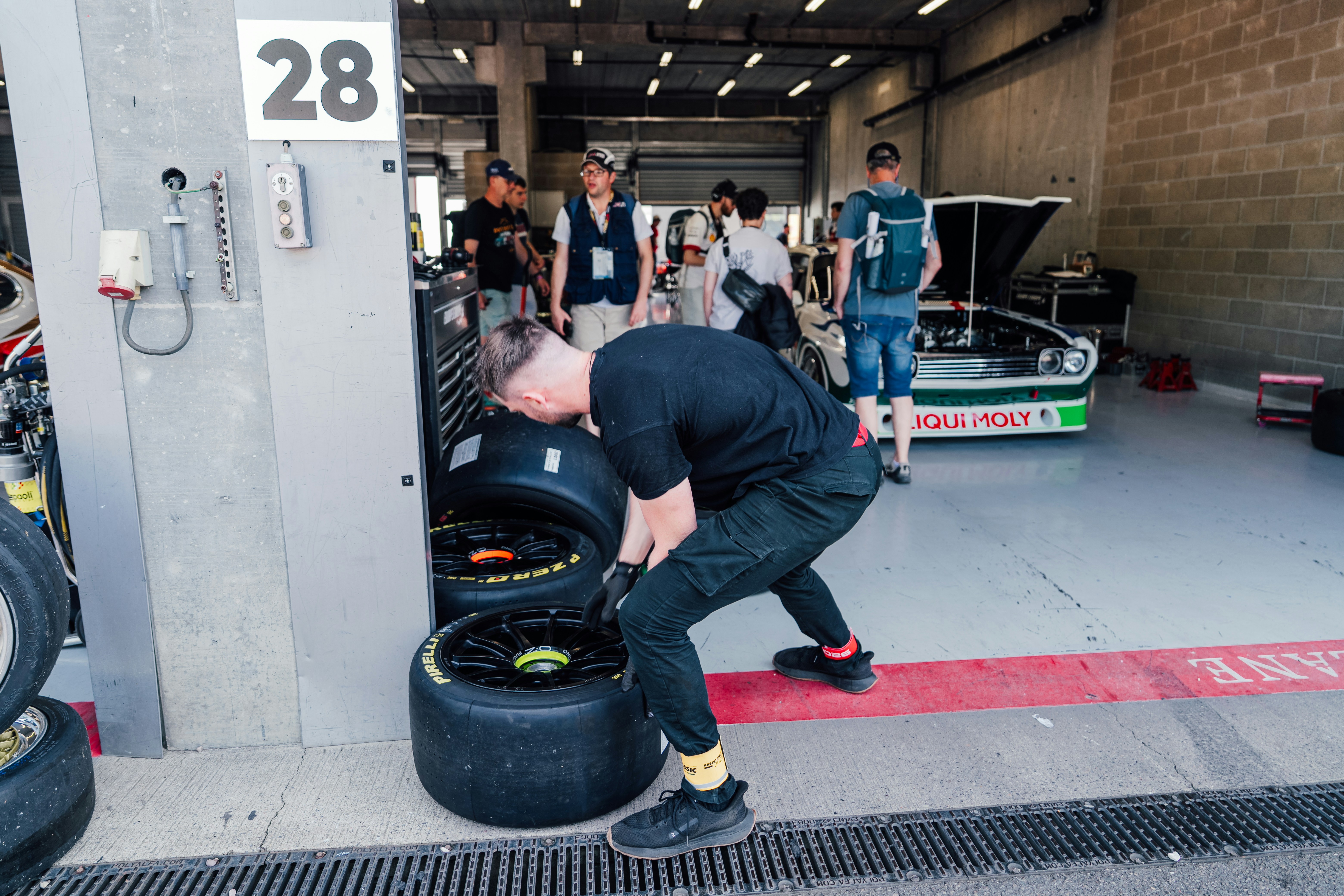 A man handles racing tires in a garage pit area.