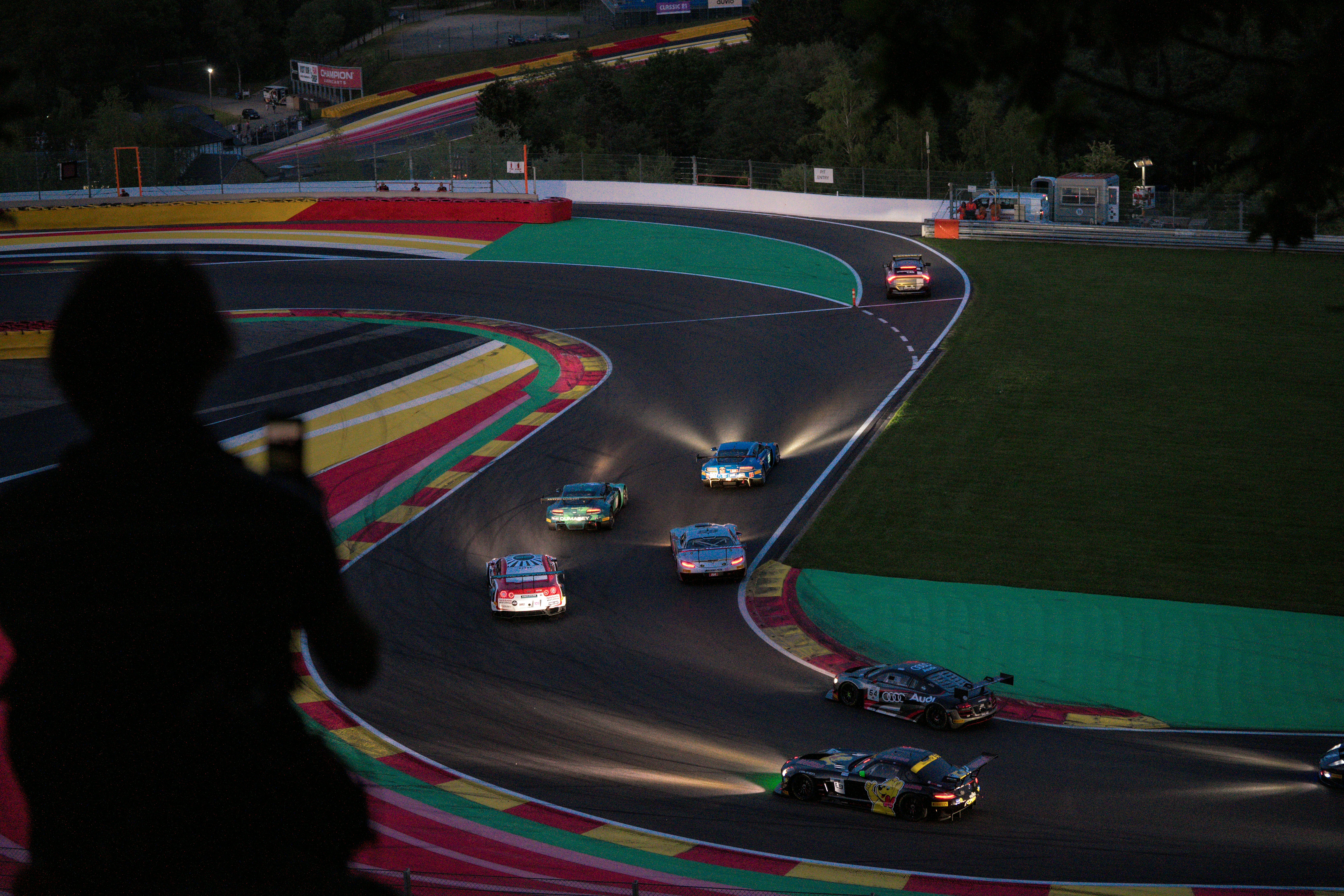 Spectator watches race cars on a track at night.