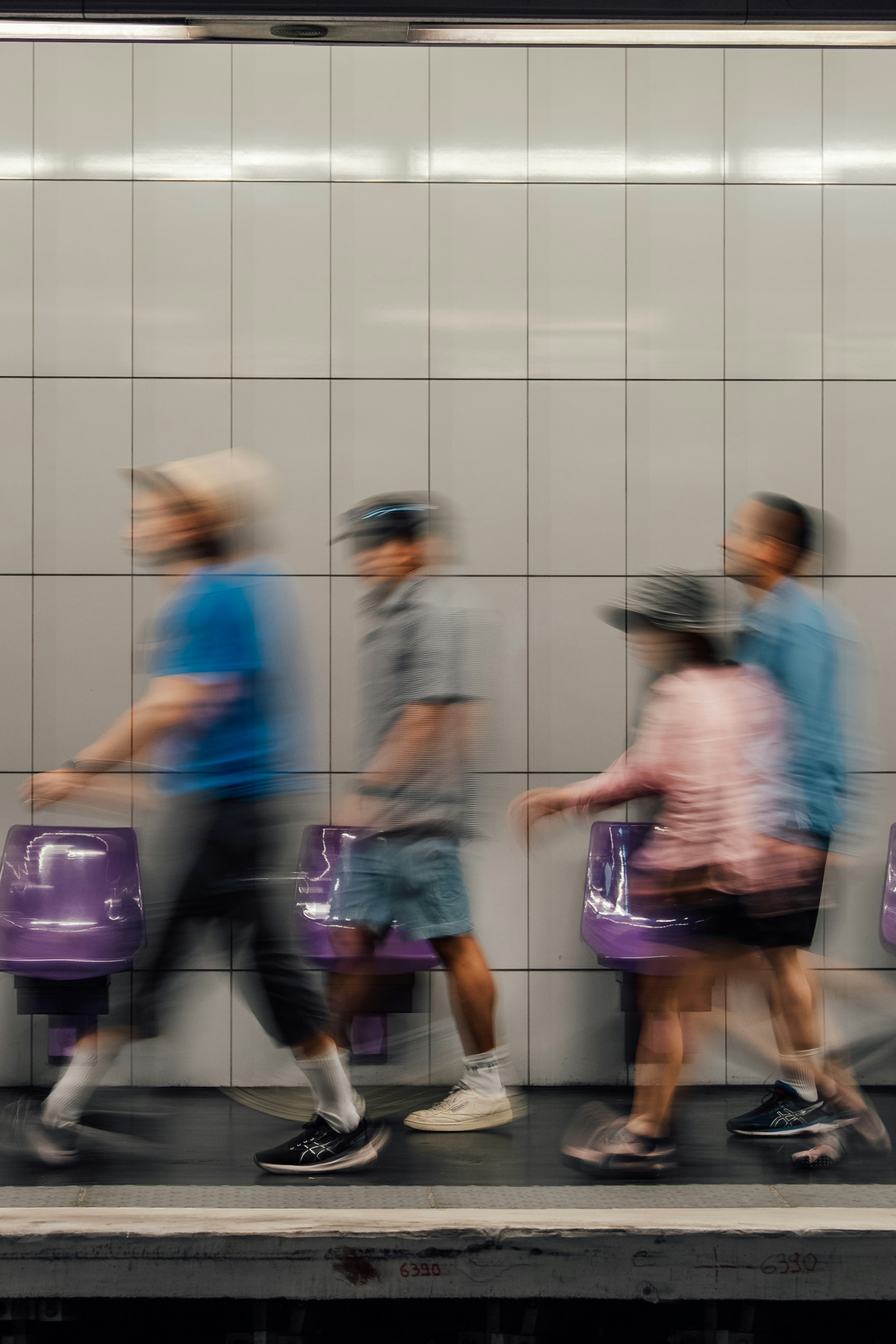 Blurry people walk past purple seats in a subway station.