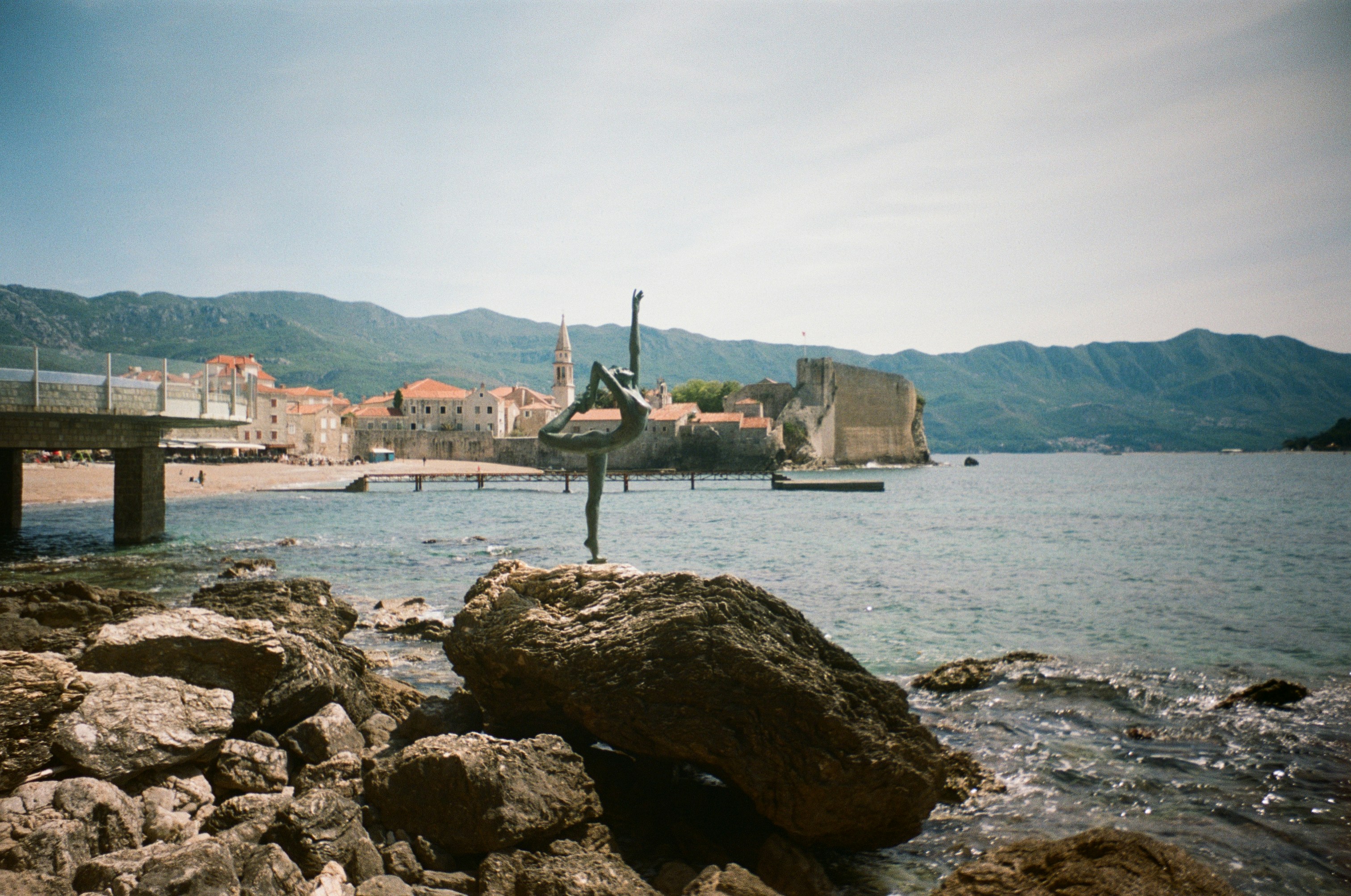 Bronze ballerina statue on rocks by a coastal town.