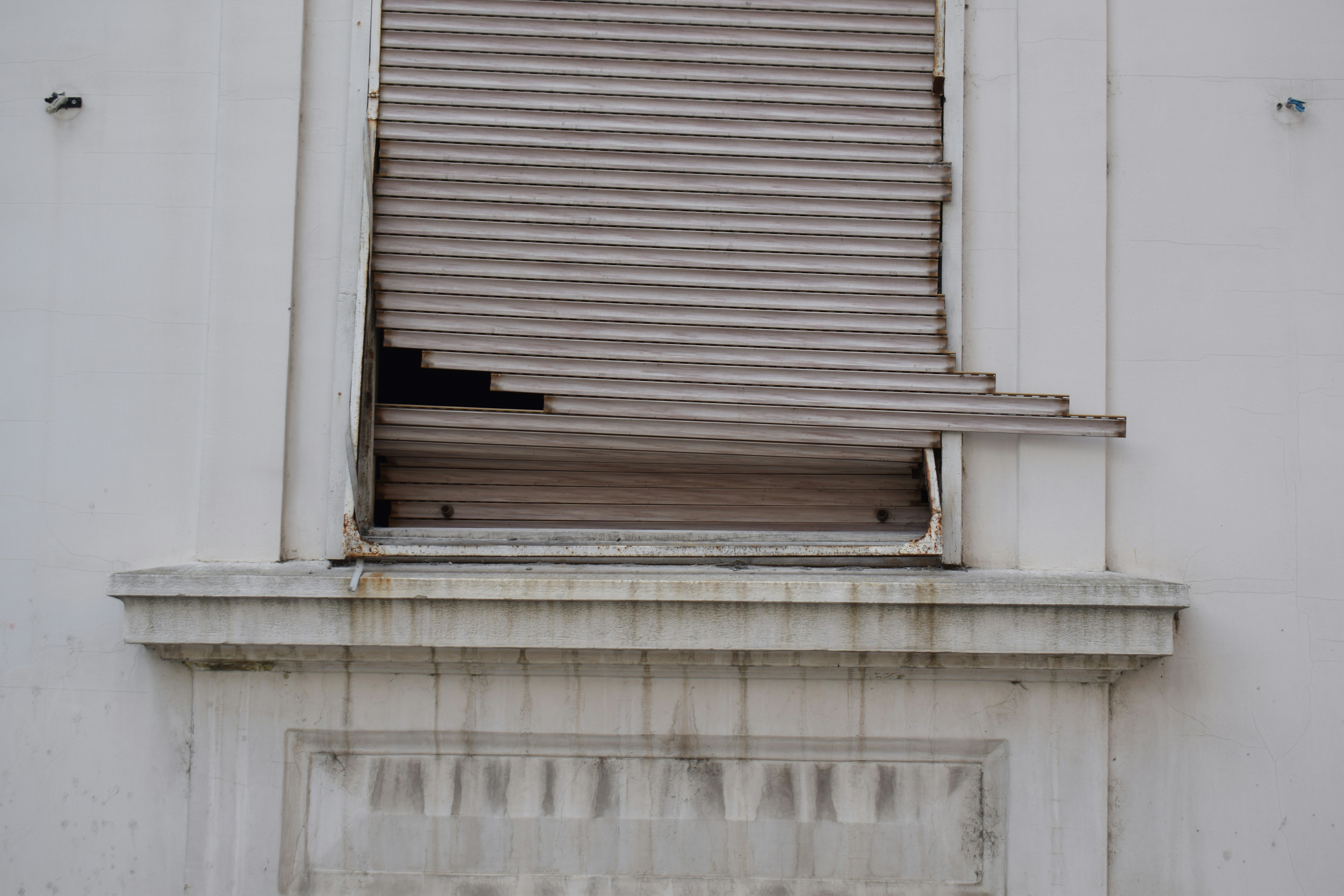 A broken window shutter on a white building facade.