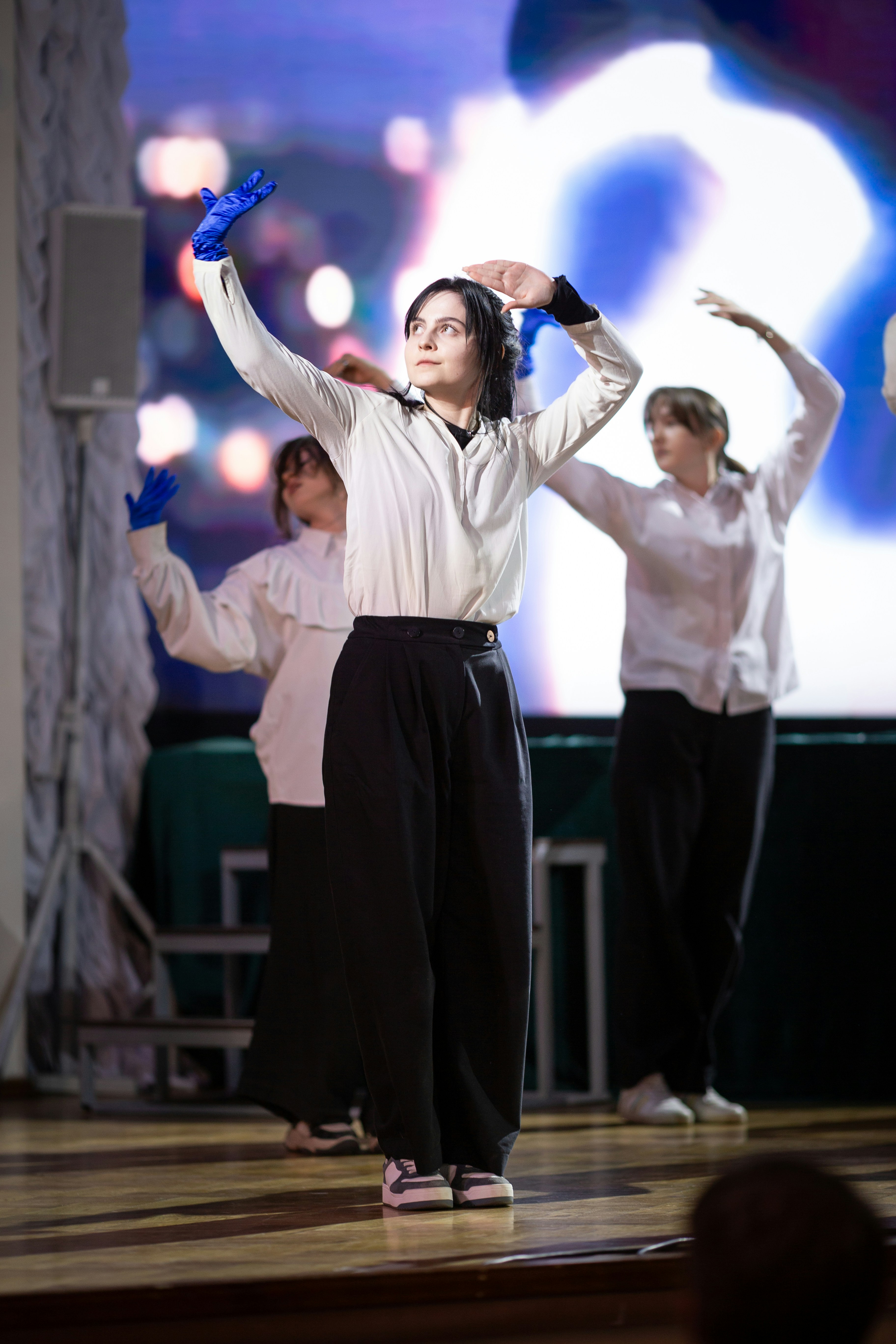 Woman in blue gloves dancing on stage with other performers.