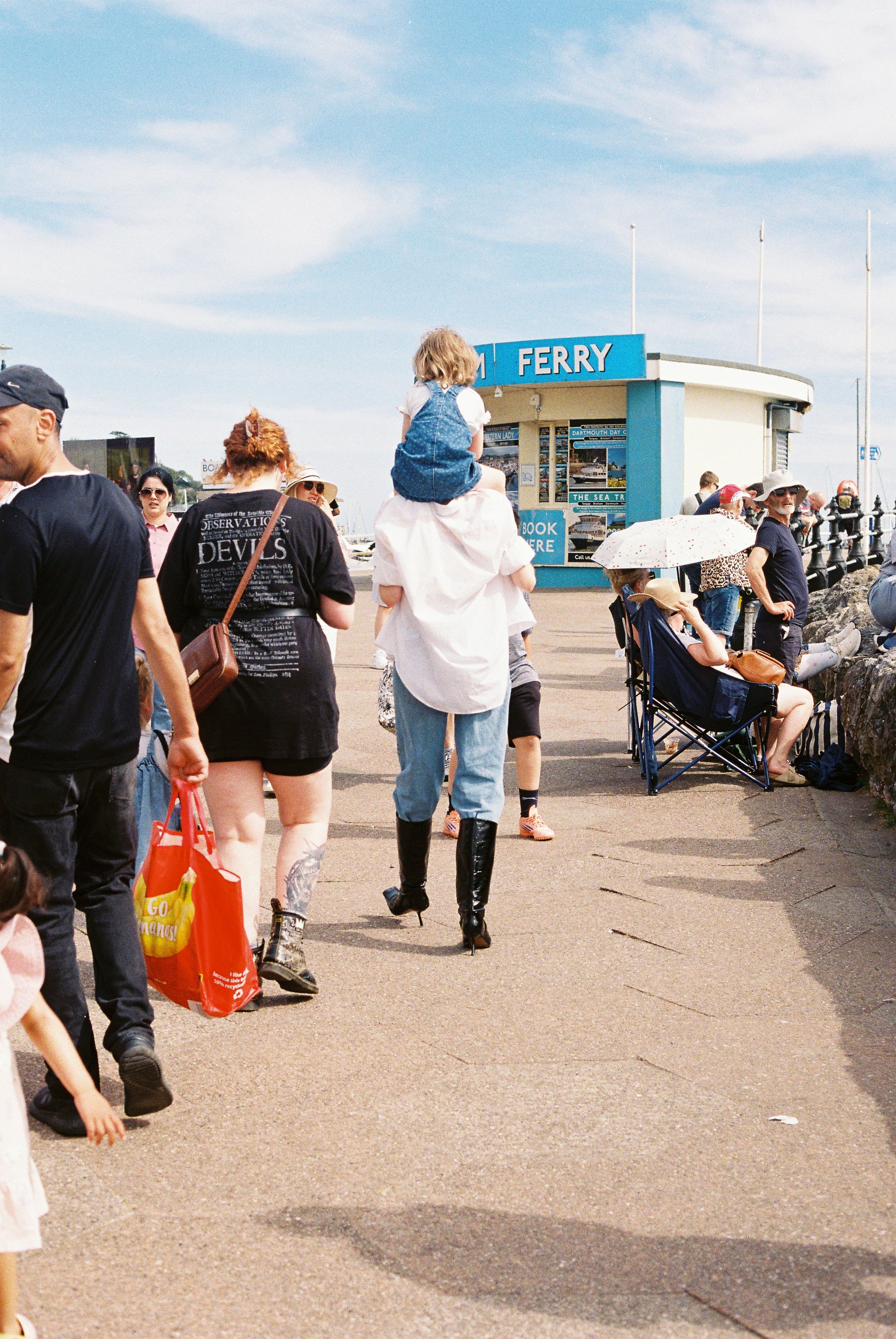 Child on shoulders walks past a ferry booth.