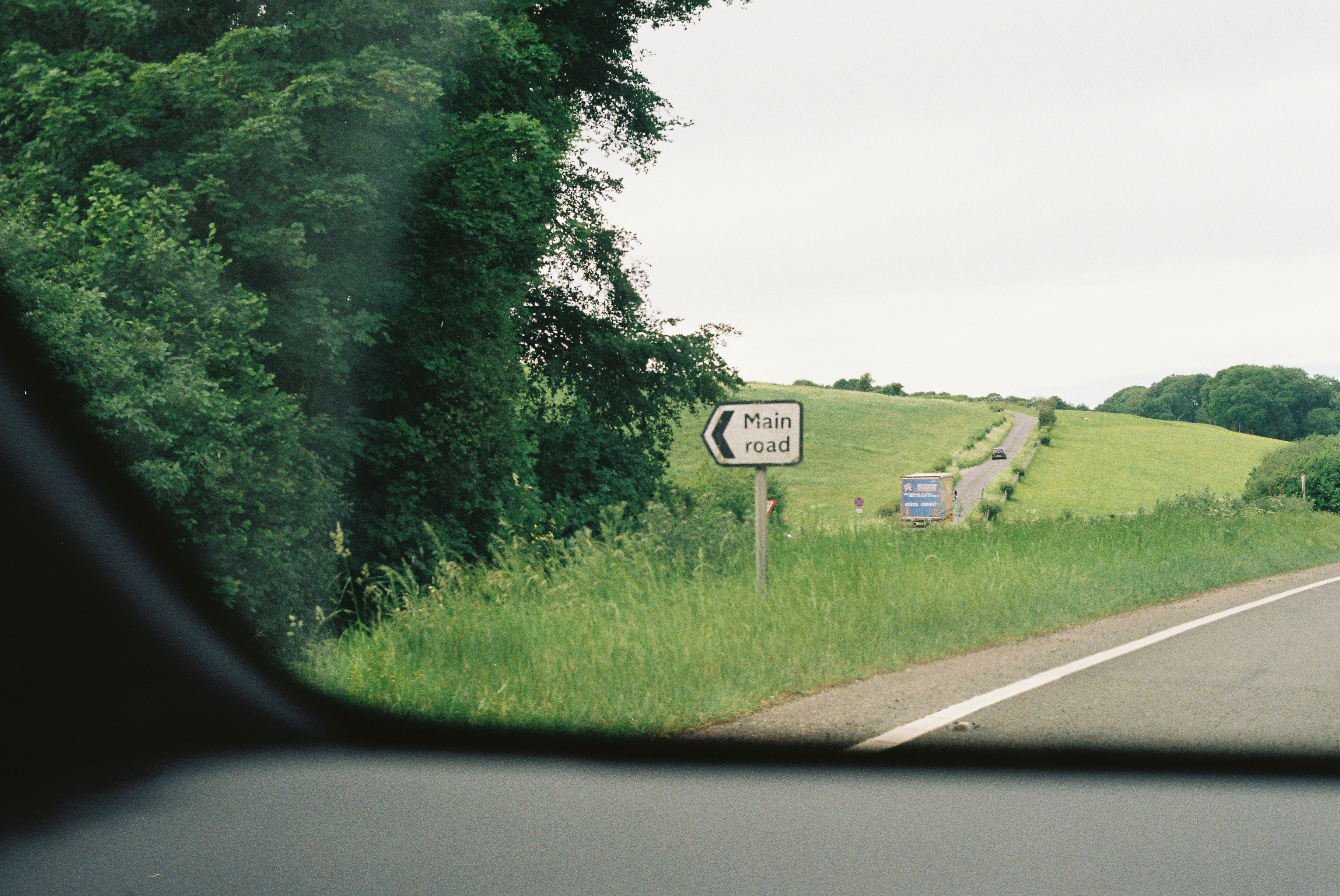 Road sign for "main road" beside a green landscape.