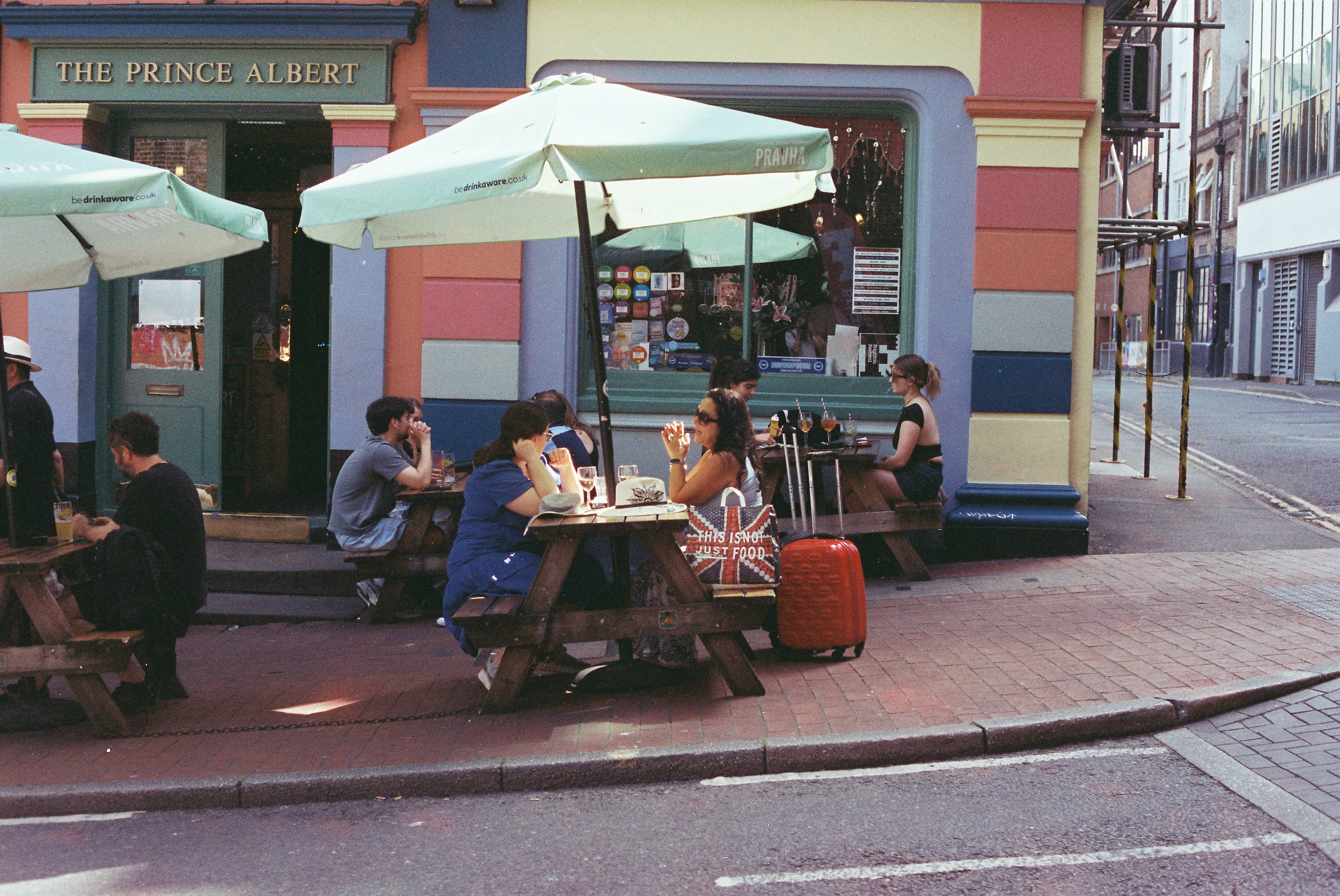 People enjoy drinks outside a colorful pub with umbrellas.