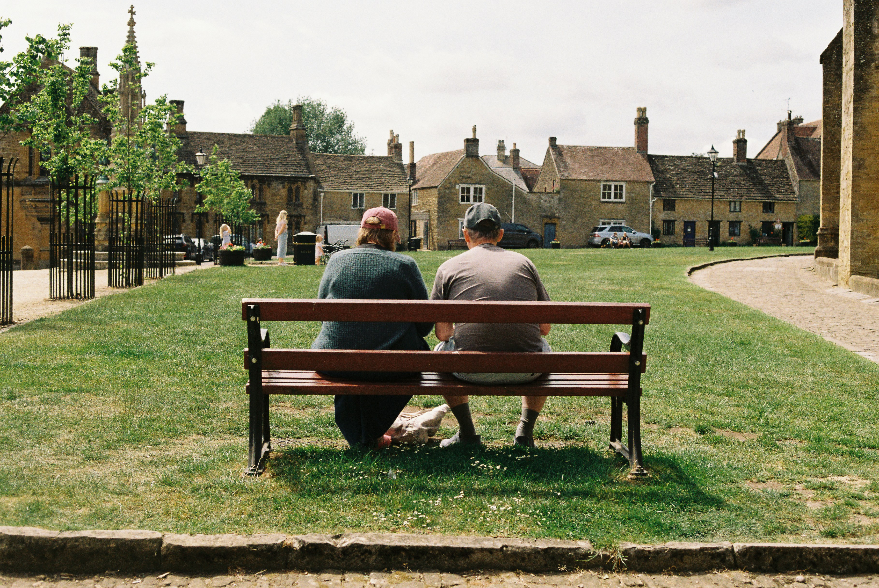 Two people sitting on a bench in a village square.