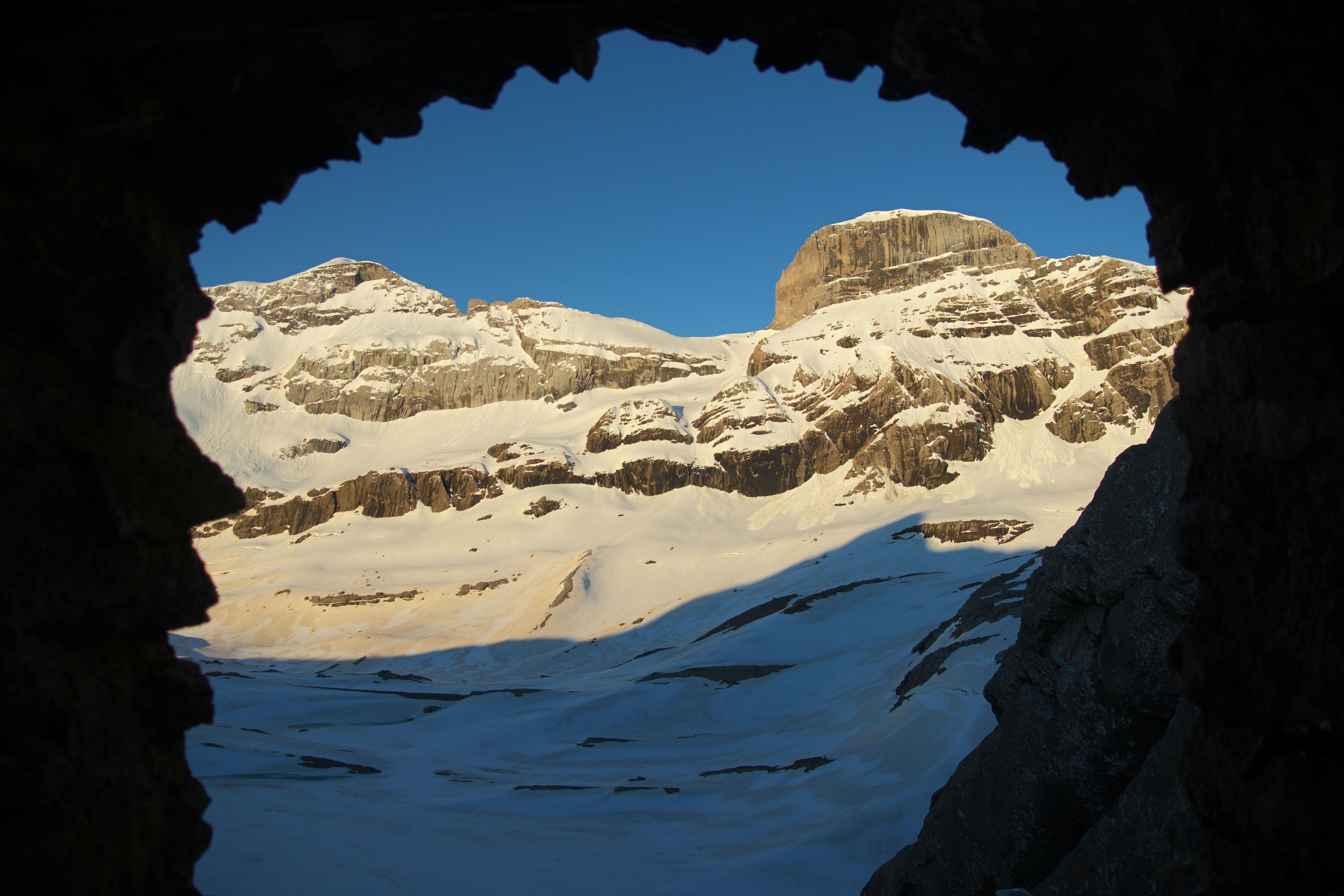 Snow-covered mountains viewed through a dark cave opening.