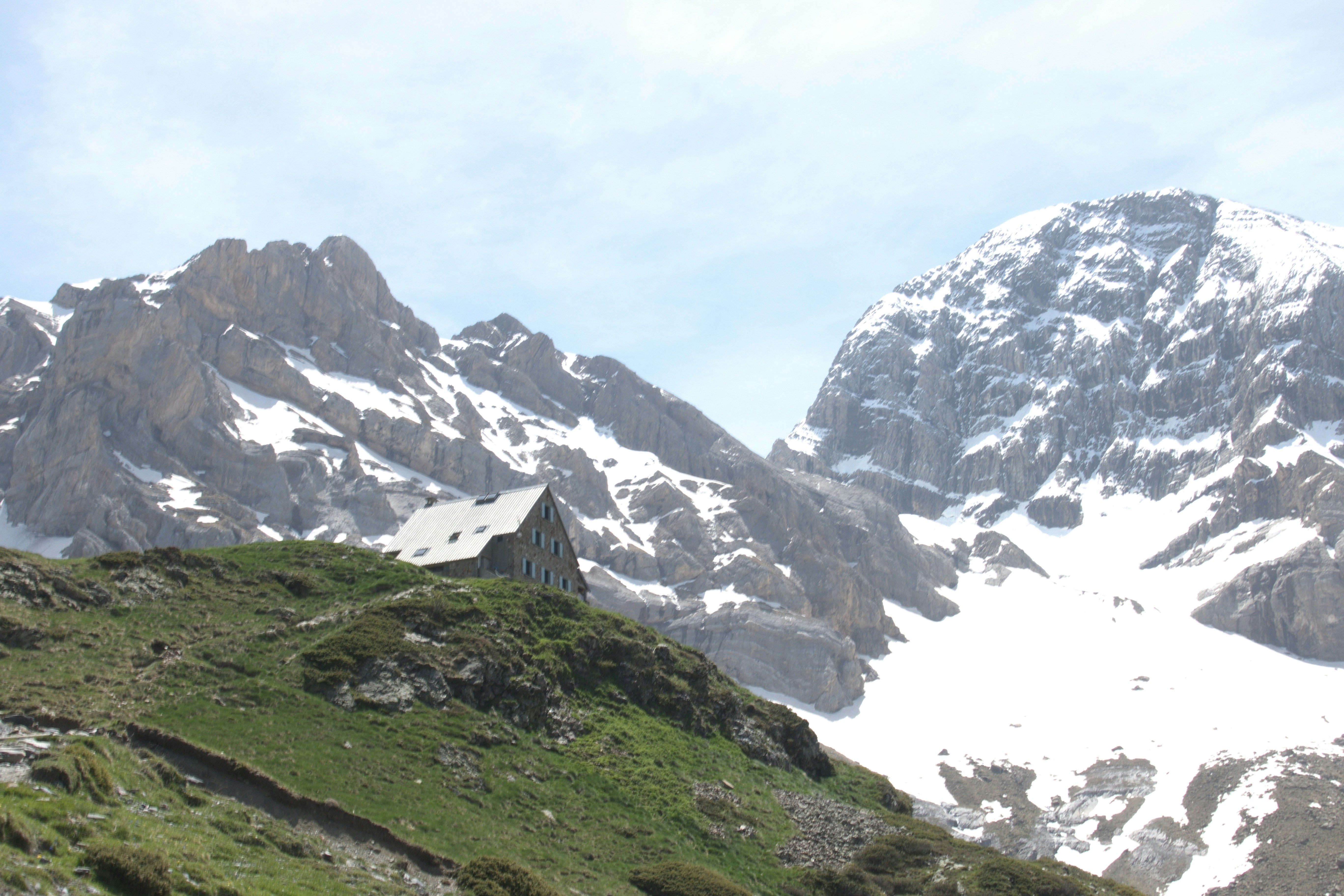 A small building on a green hill with snowy mountains.