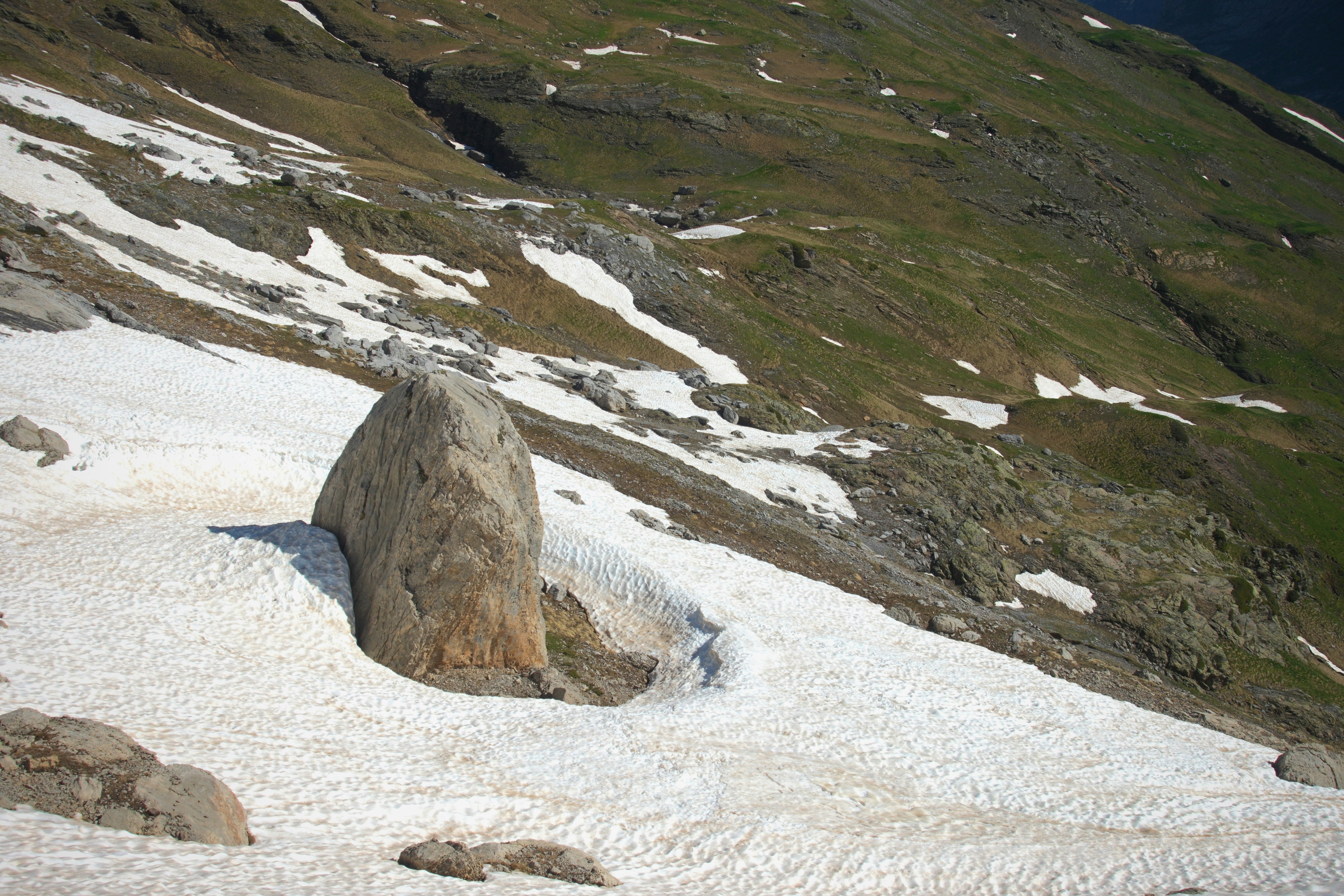 Large rock on a snowy mountain slope with green patches.