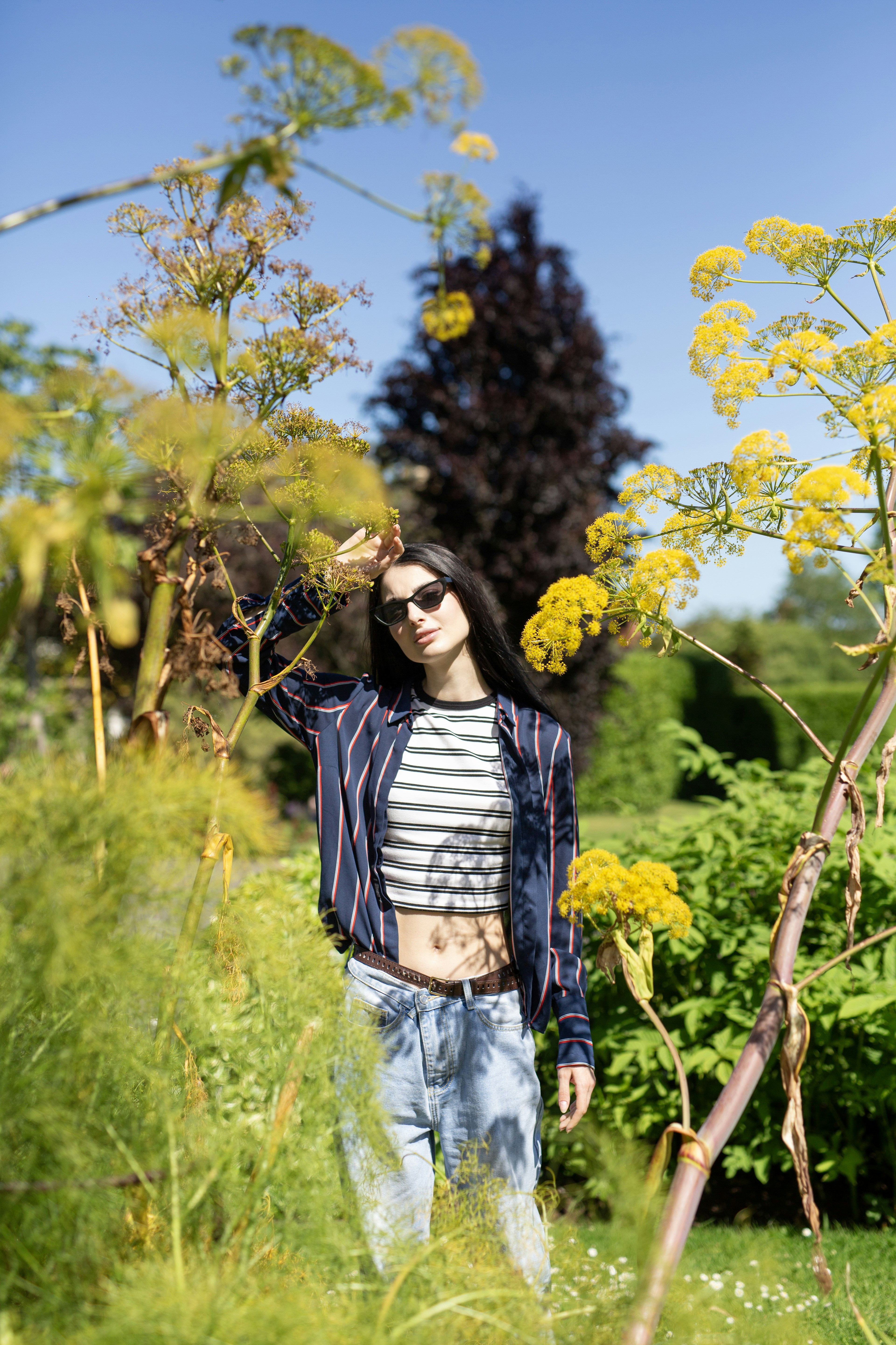 Stylish woman in sunglasses standing amidst vibrant yellow plants.