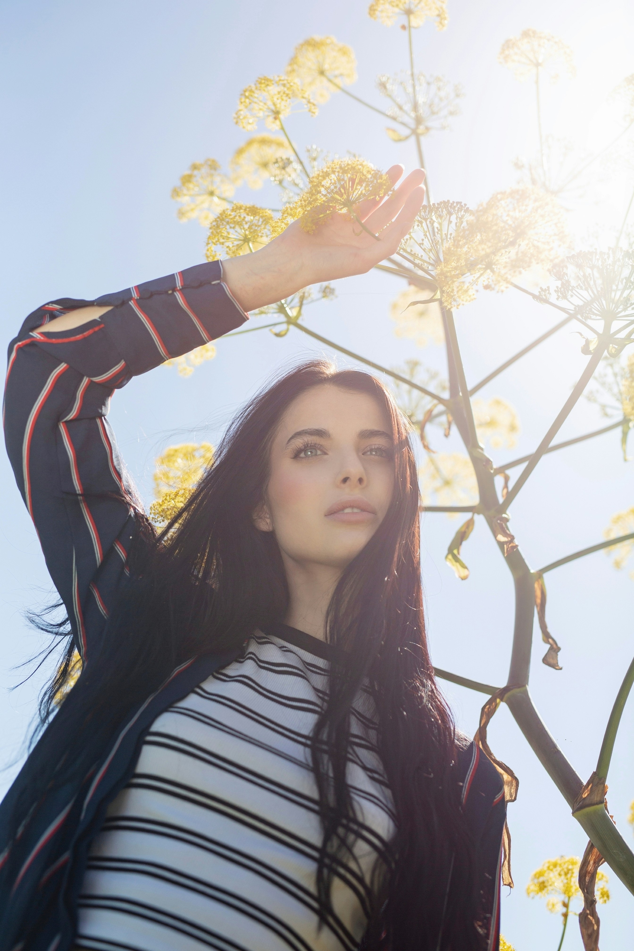 Young woman near yellow flowers, shielding eyes from bright sun.