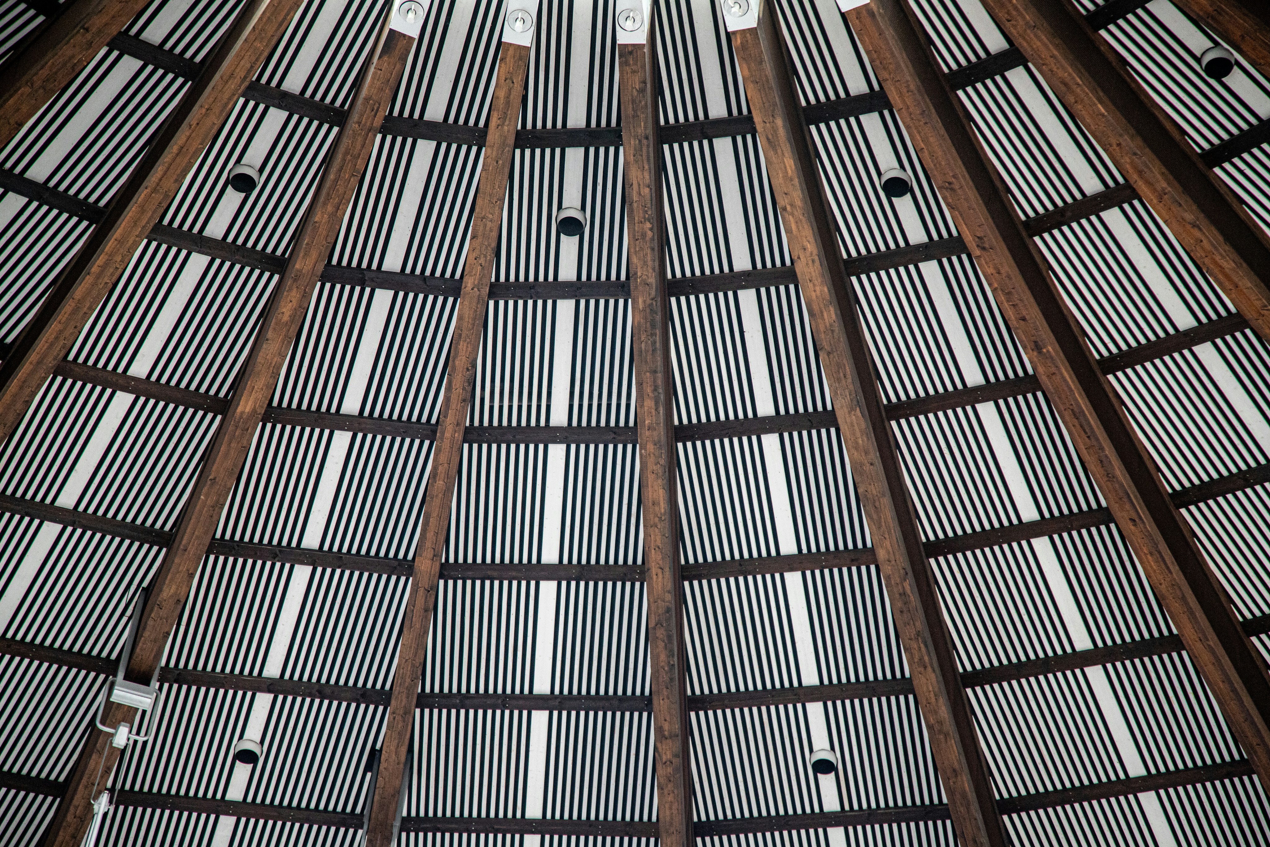 Conical roof interior with wooden beams and striped ceiling panels.