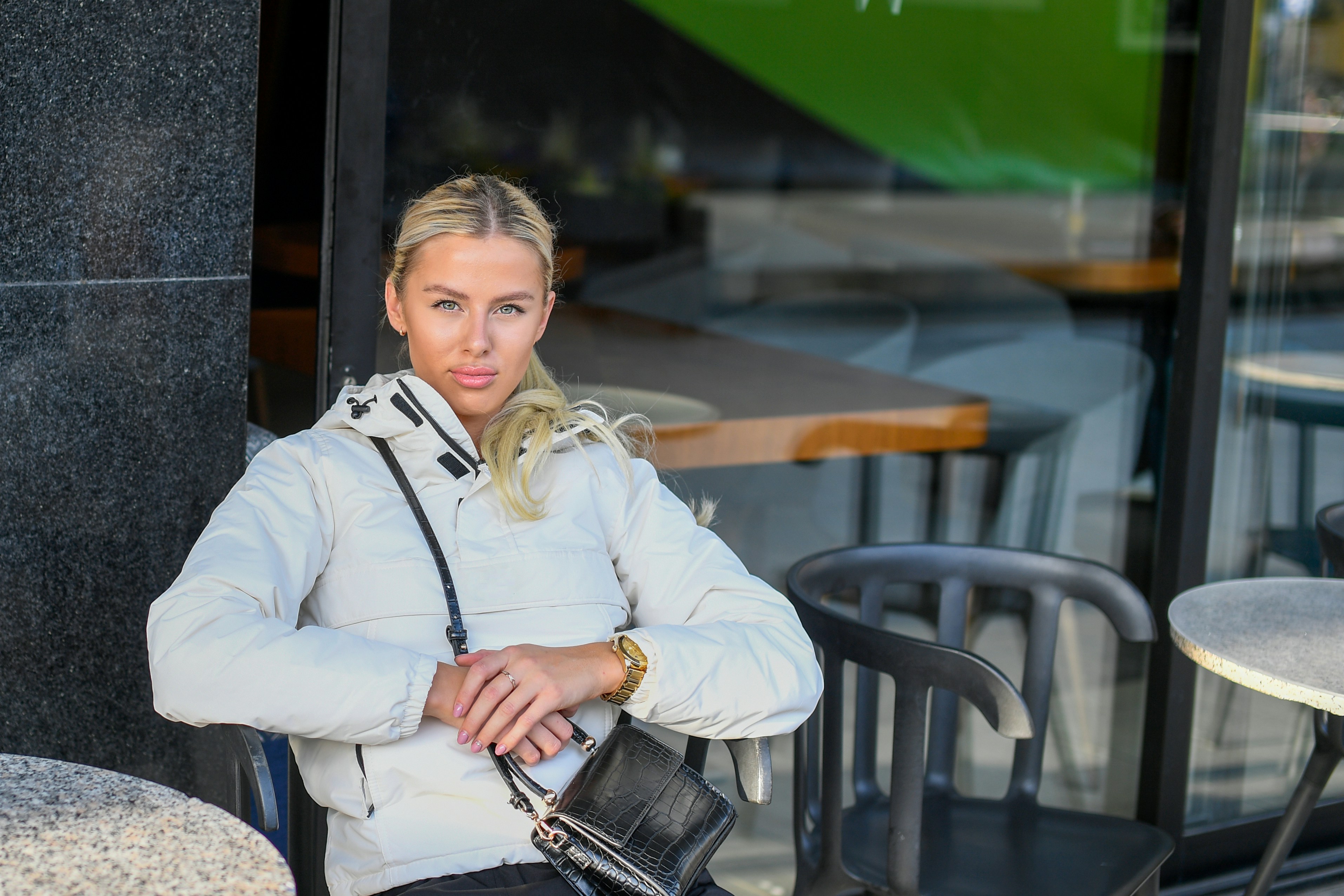 Blonde woman in a puffer jacket sitting outside a cafe.