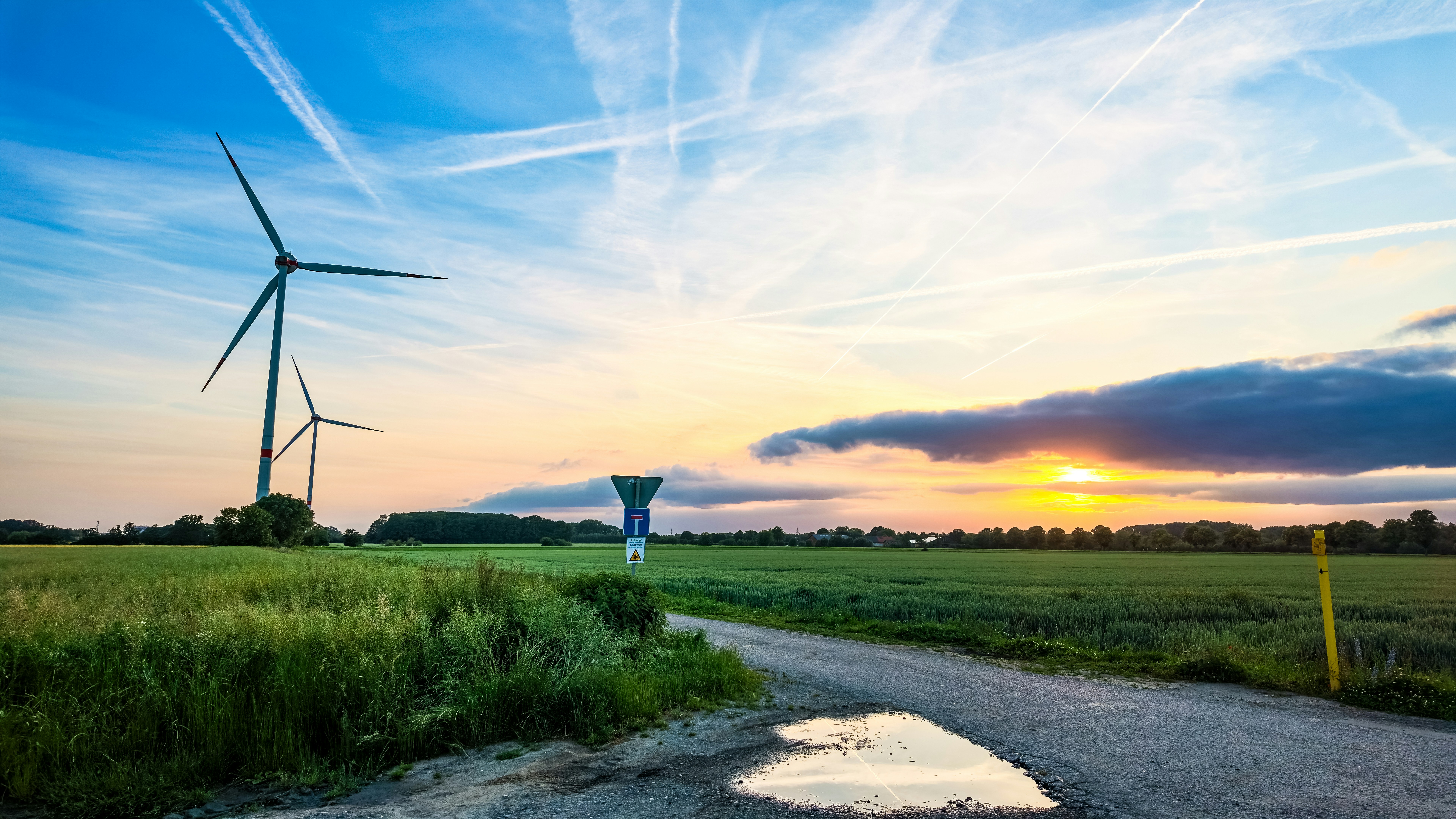 Green field with wind turbines and a colorful sunset sky.