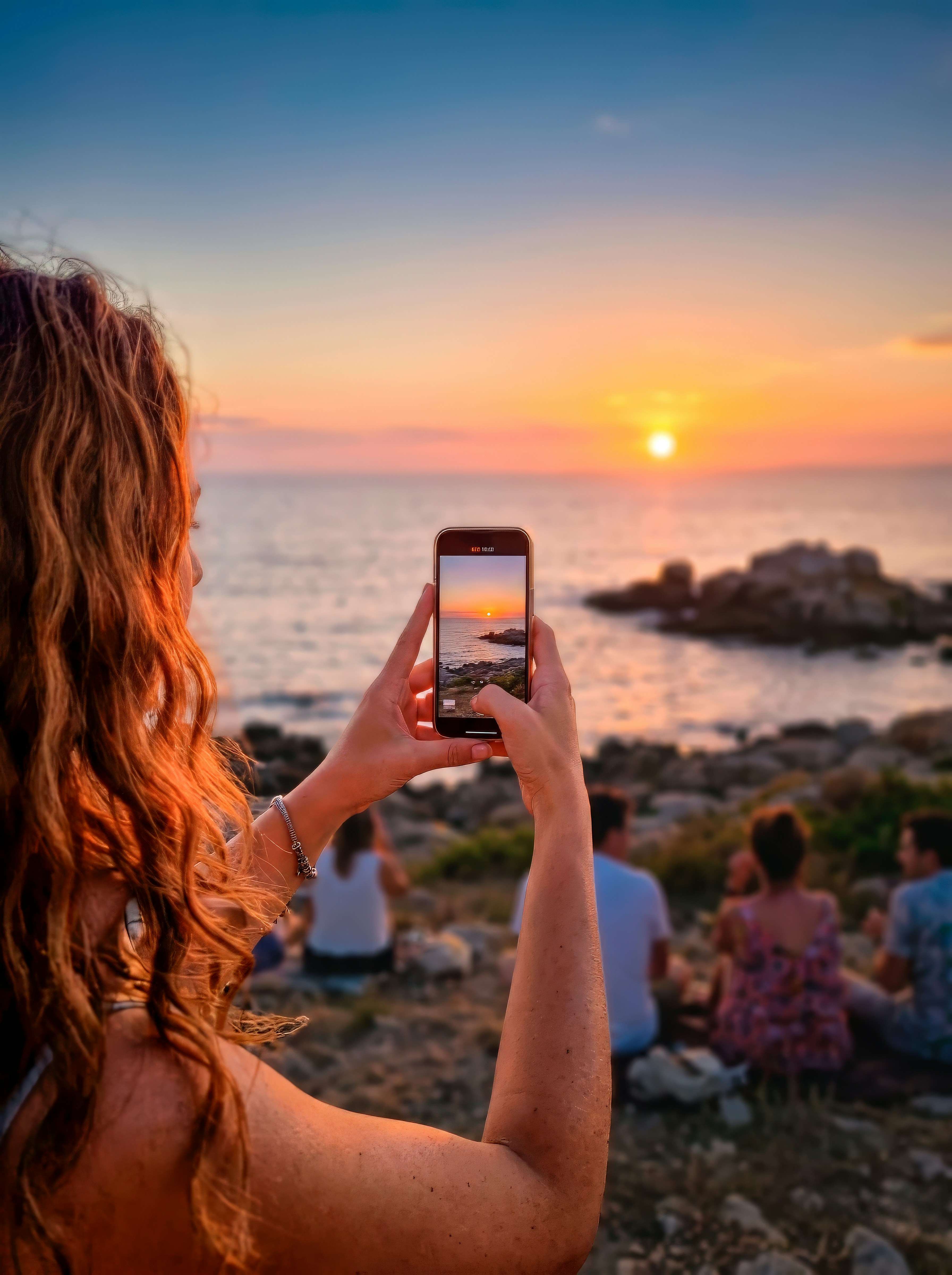 Woman photographs stunning ocean sunset with her smartphone.
