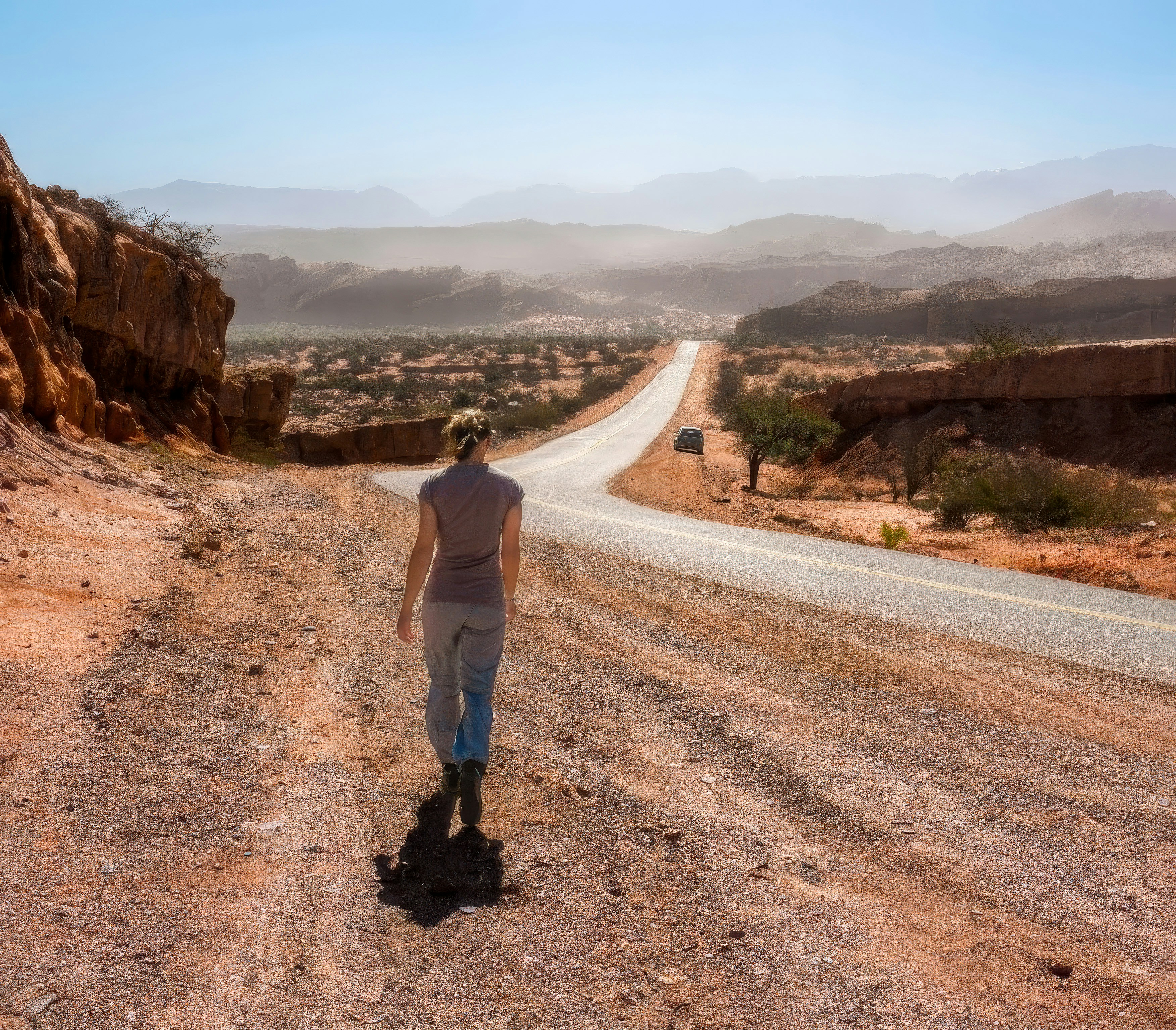 Woman walking on a dirt path beside a desert road.