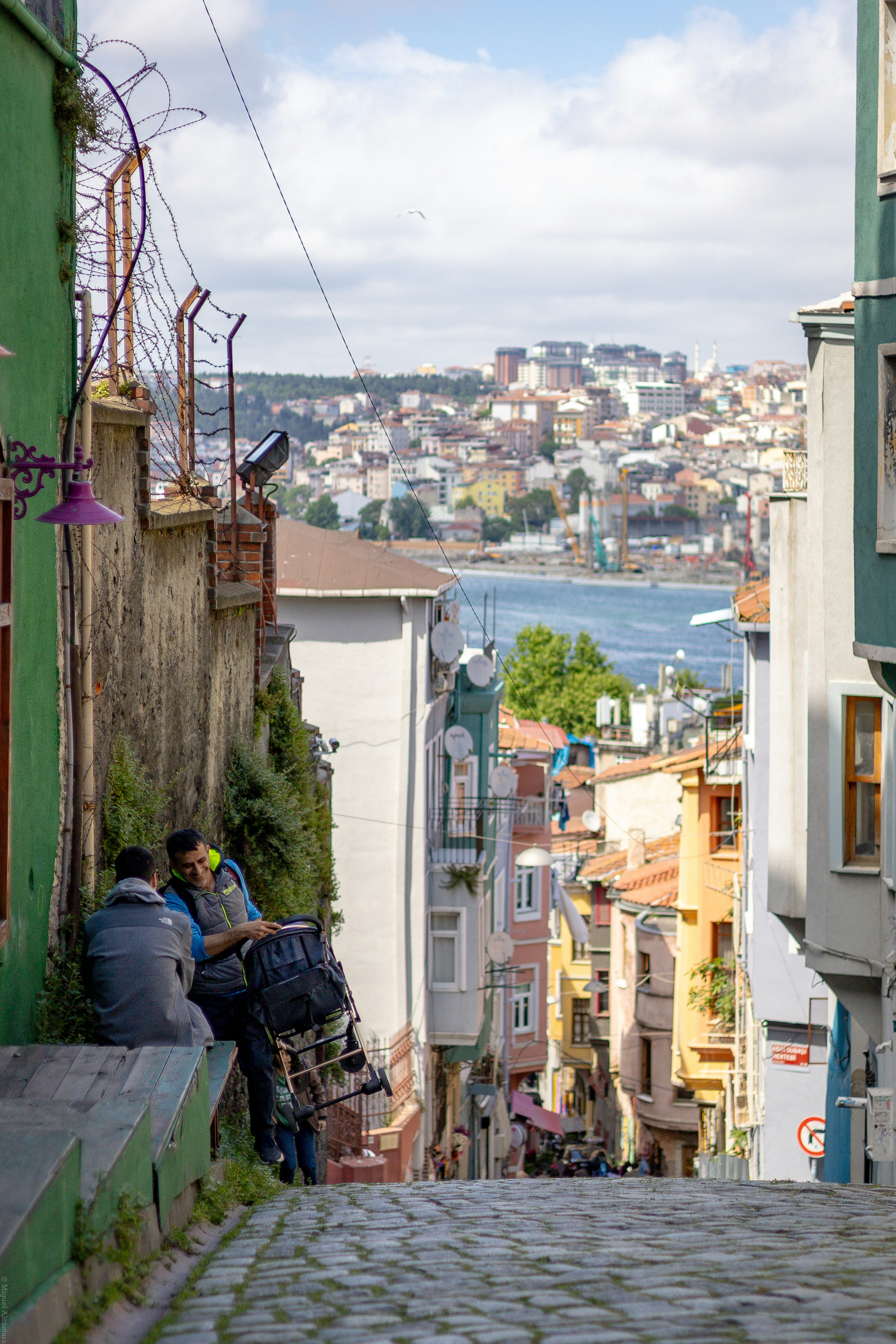 Two men resting on steep cobblestone street with city view.