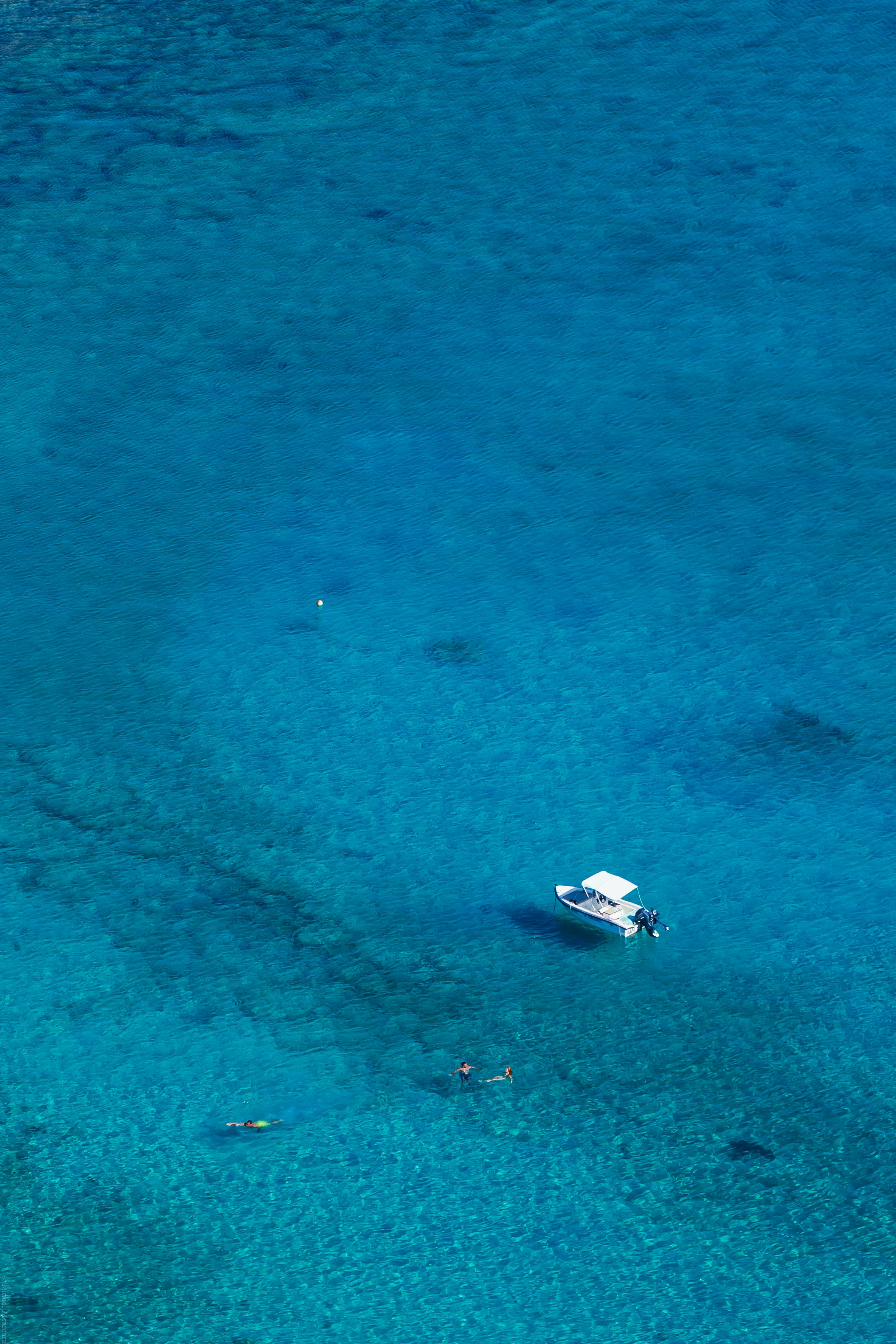Aerial view of a boat and snorkelers in blue water.