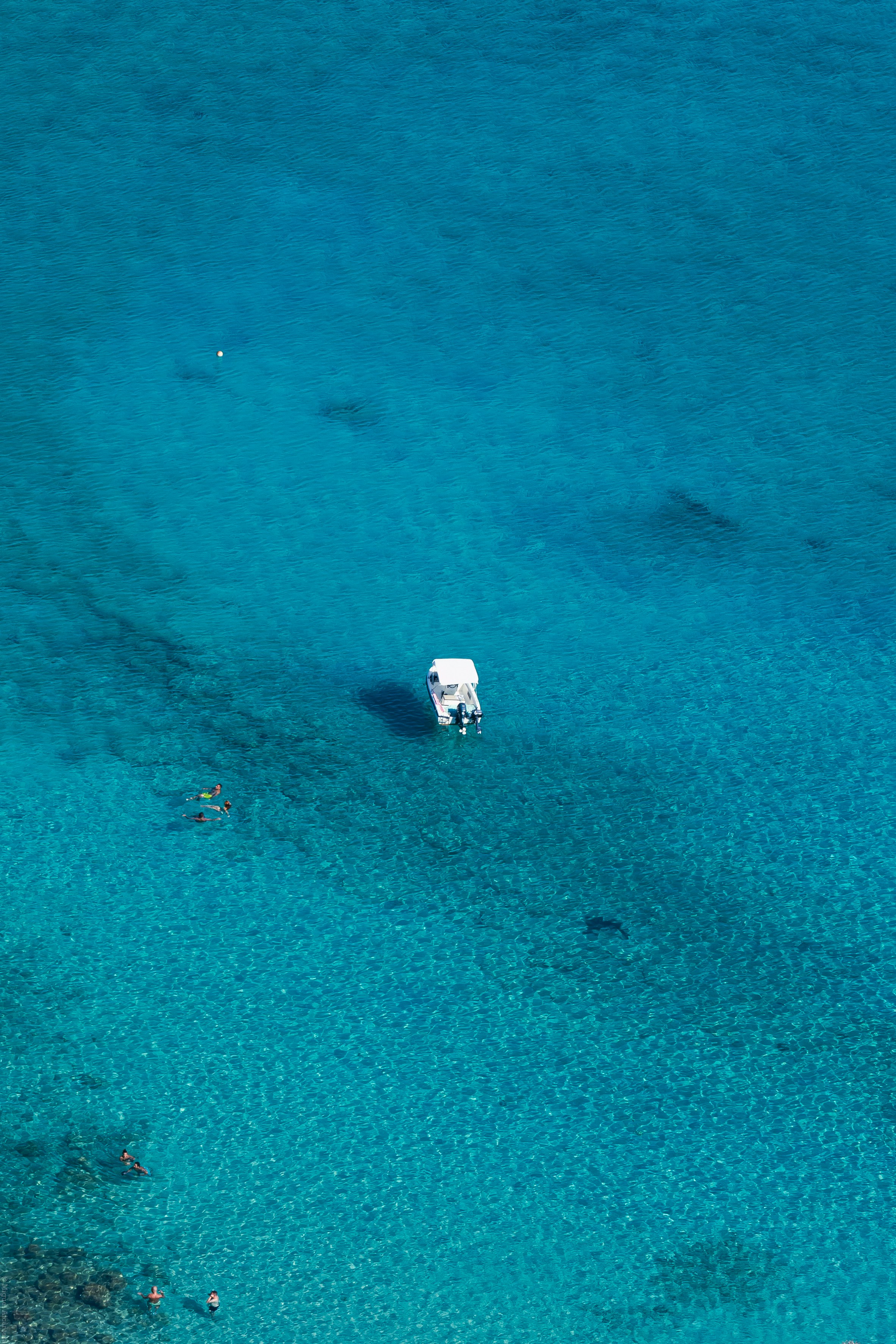 White boat in clear blue ocean water with seabed visible.