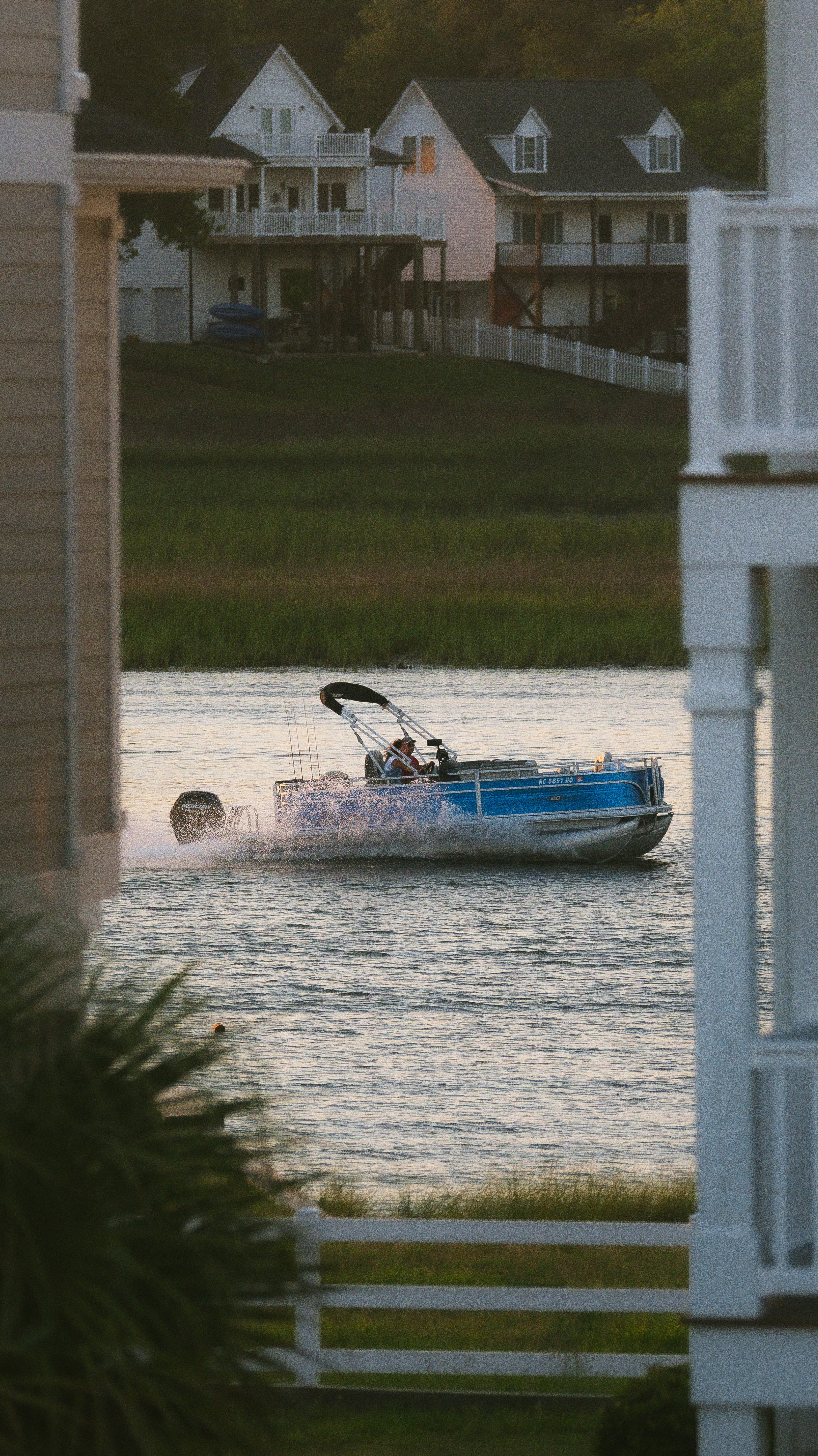Blue pontoon boat speeding past waterfront houses.