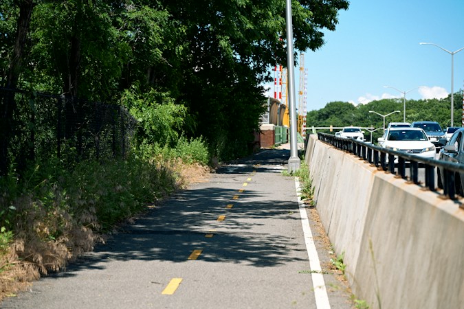 Sunny paved walking and bike path running beside a busy highway, similar to the trail connections being built across the 215 Beltway