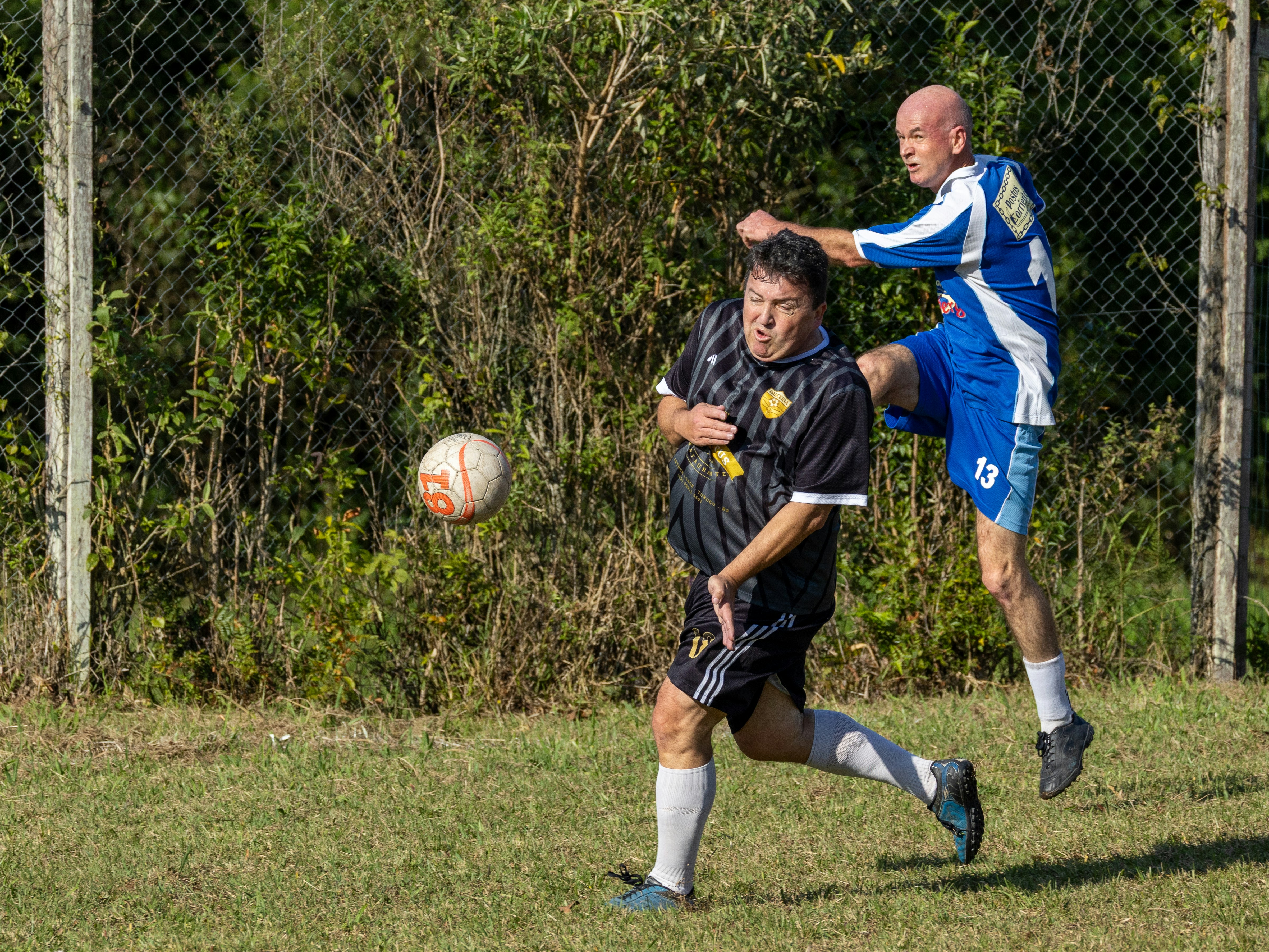 Two men playing soccer, one jumping to kick the ball